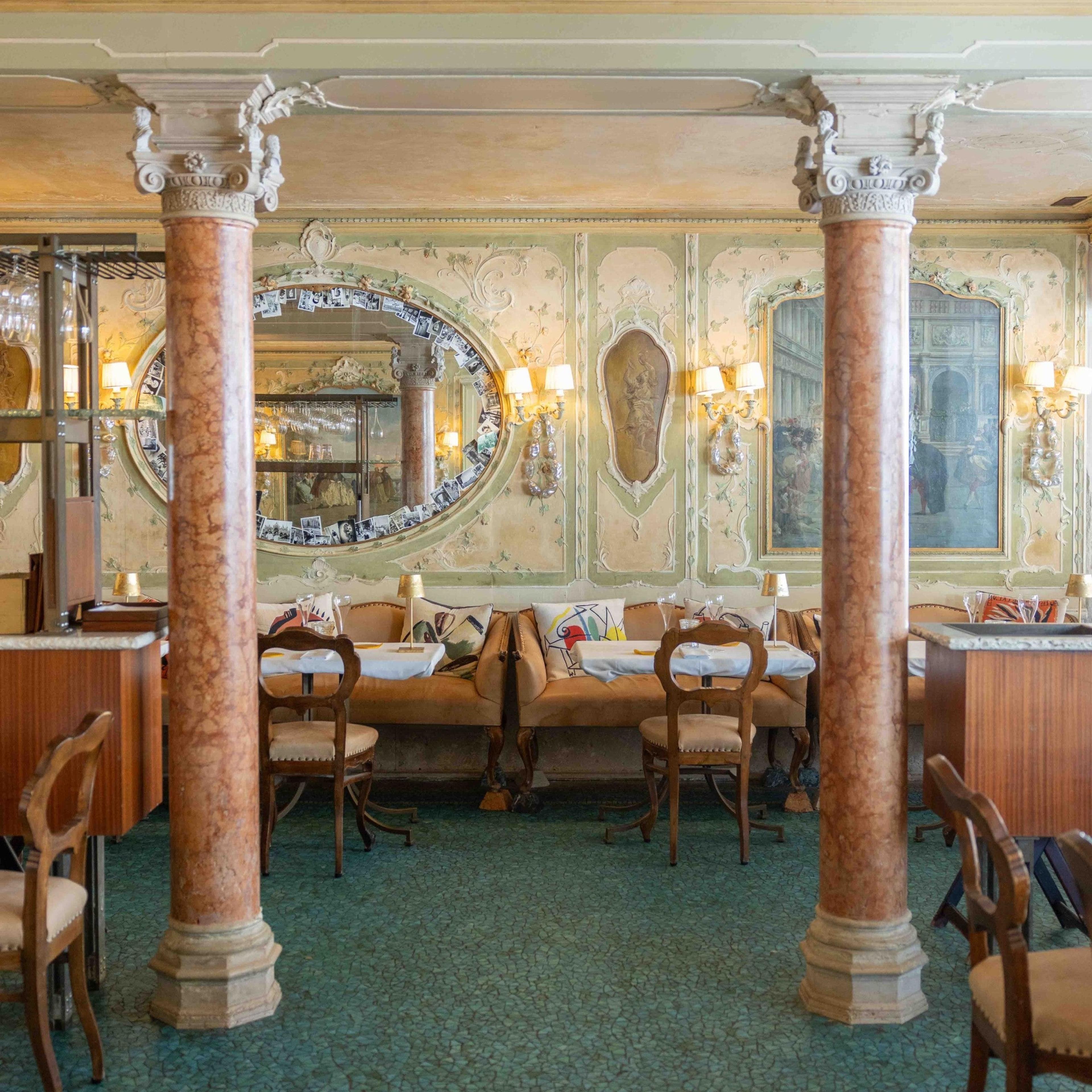 An ornate dining room with gilded mirrors, marble columns and set tables