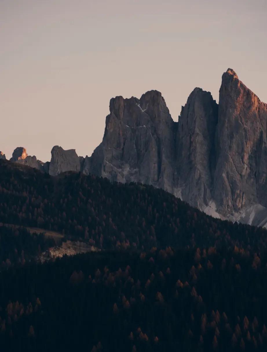 Dramatic rock peaks catch the last light above a dark forested ridge at dusk.