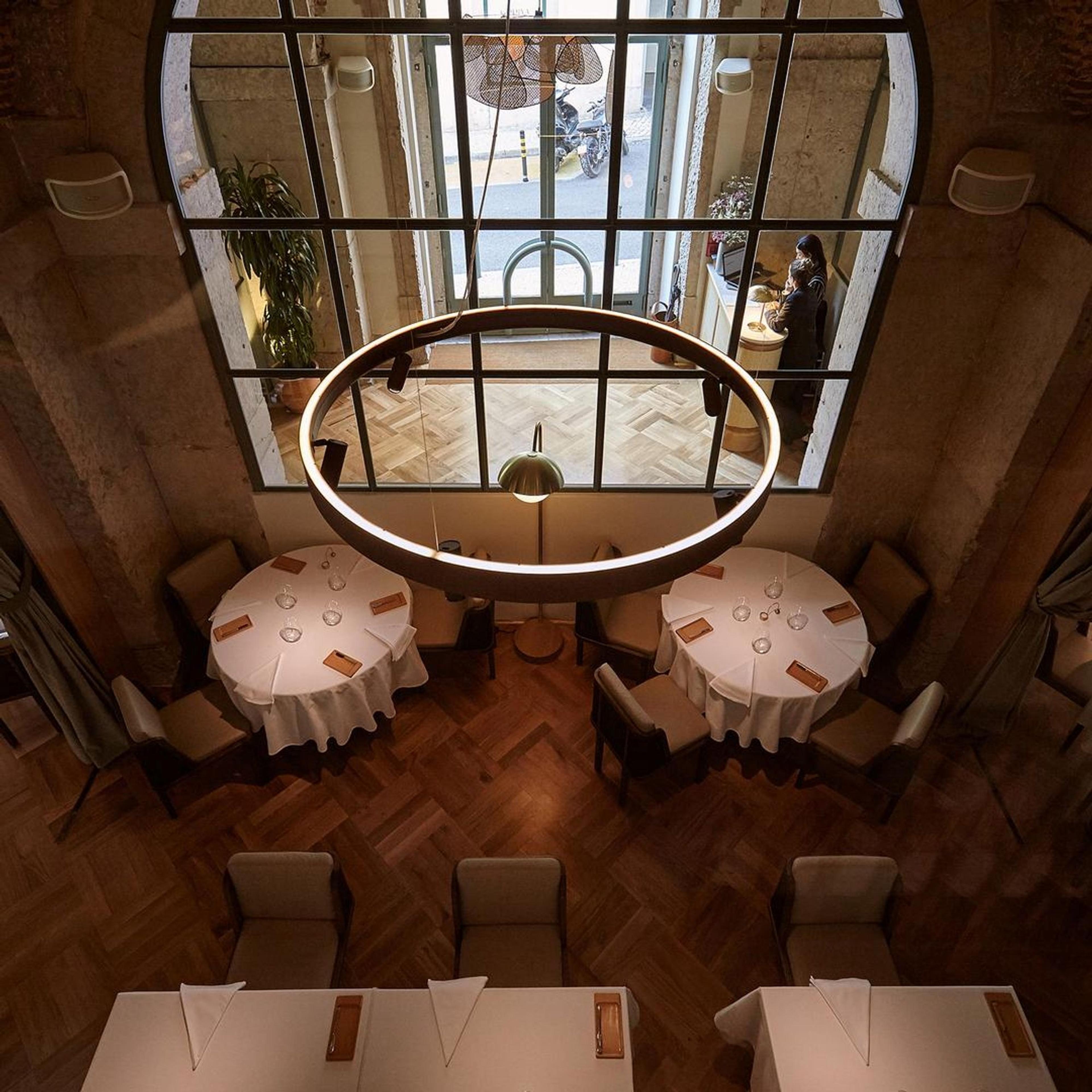 Two round tables laid in white beneath a circular light, in a room of dark wood