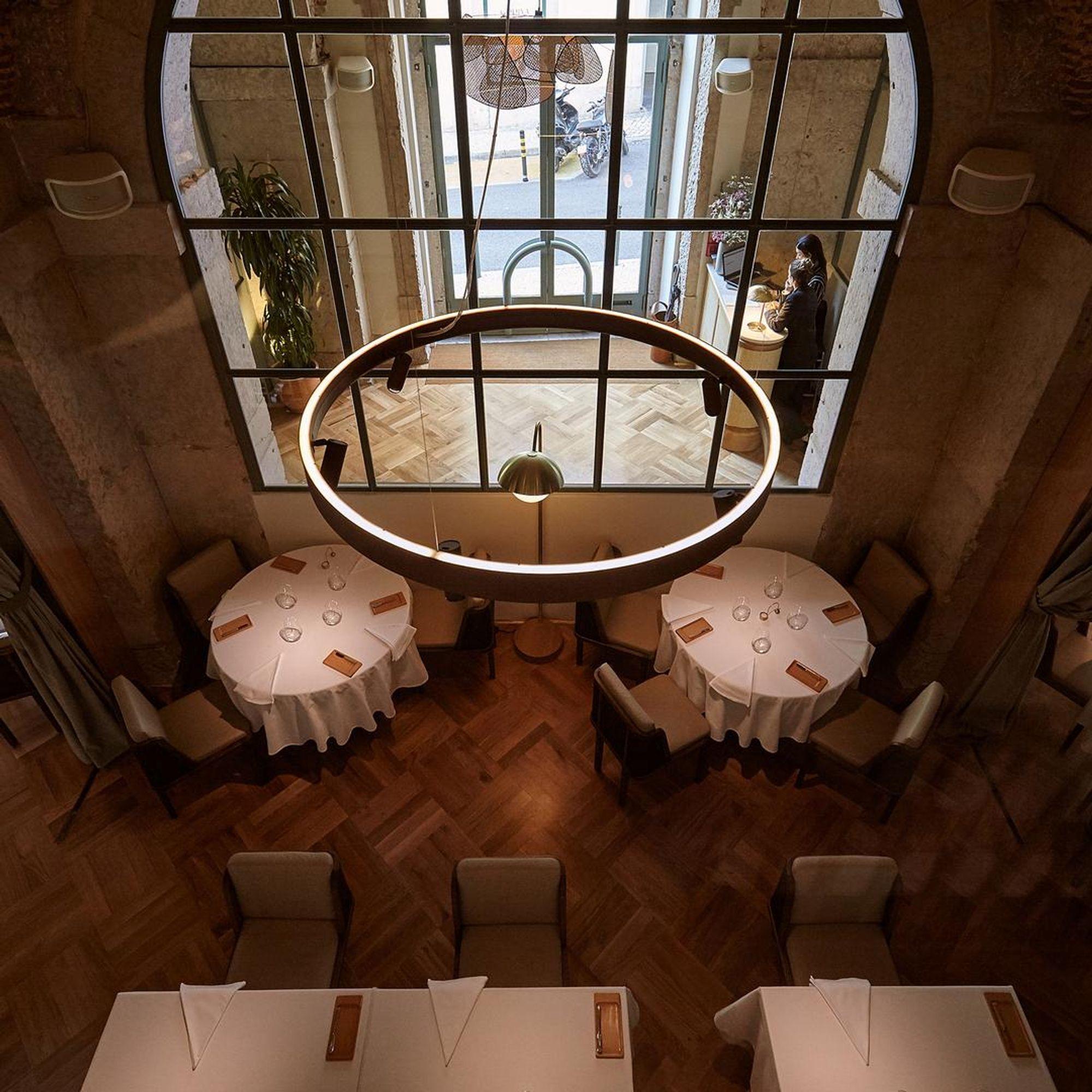 Two round tables laid in white beneath a circular light, in a room of dark wood