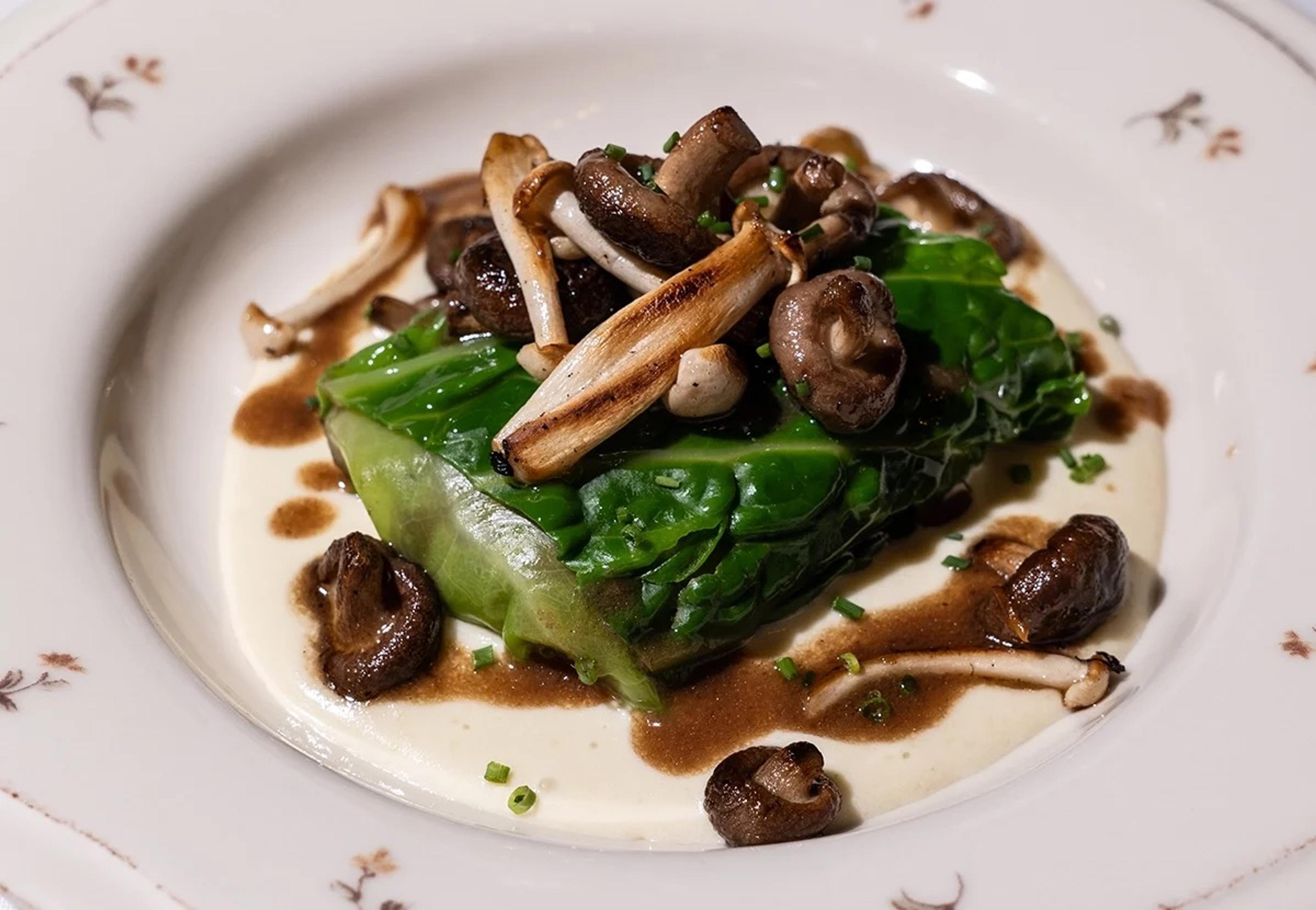 A plated dish of braised greens and roasted mushrooms over a cream sauce, on a floral-rimmed plate.
