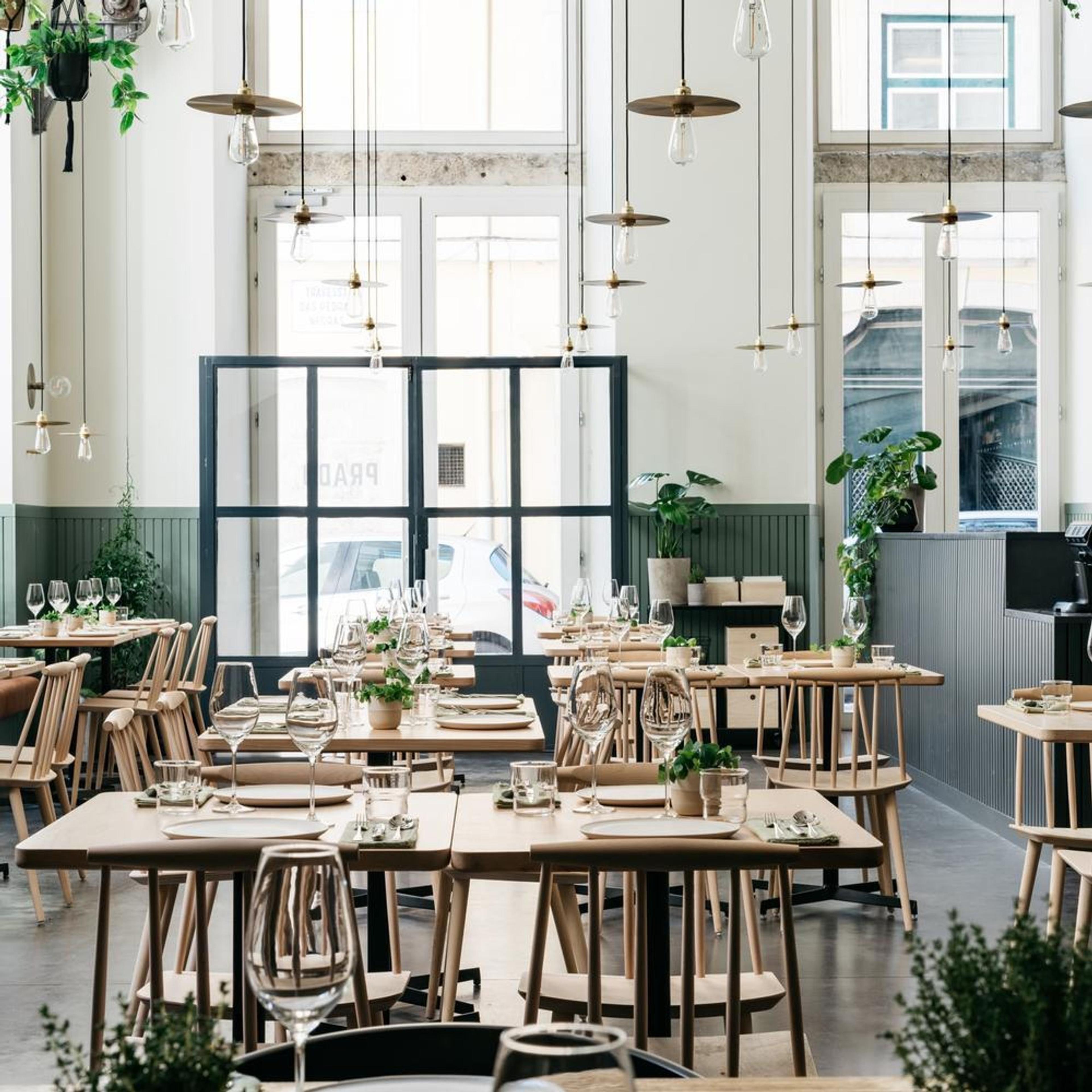 A bright dining room of wooden tables beneath tall windows