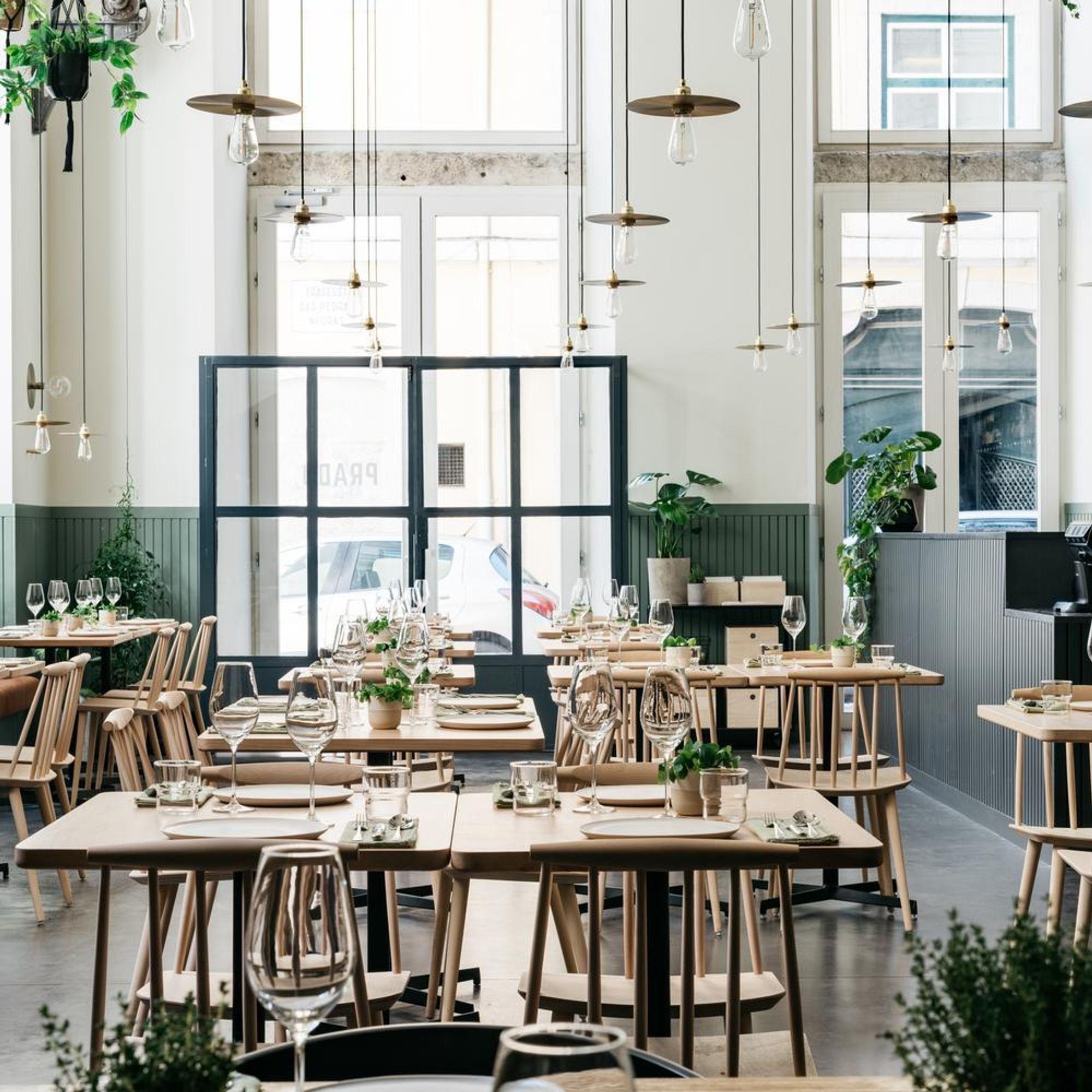 A bright dining room of wooden tables beneath tall windows