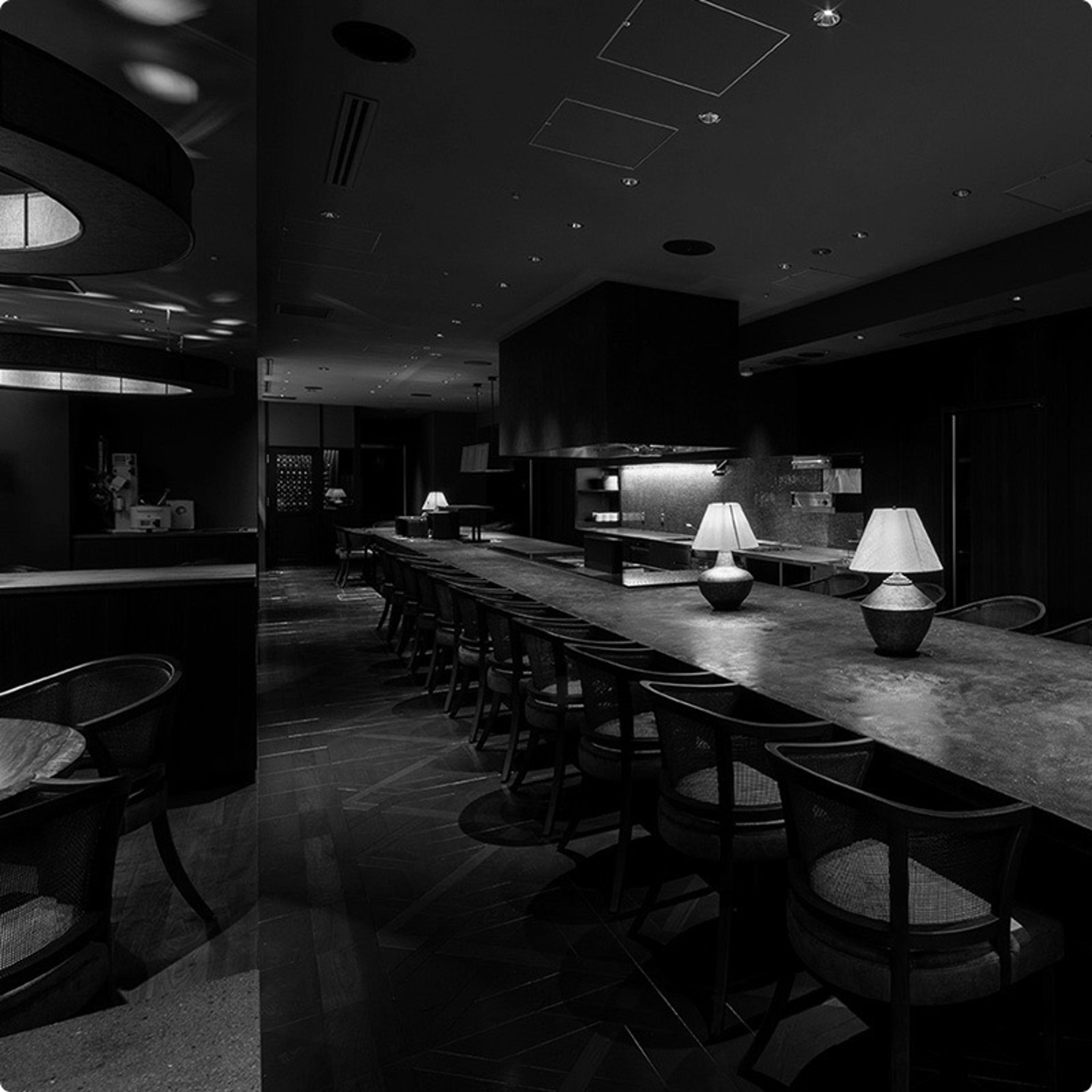 A long dark counter facing the open kitchen, lit by small table lamps