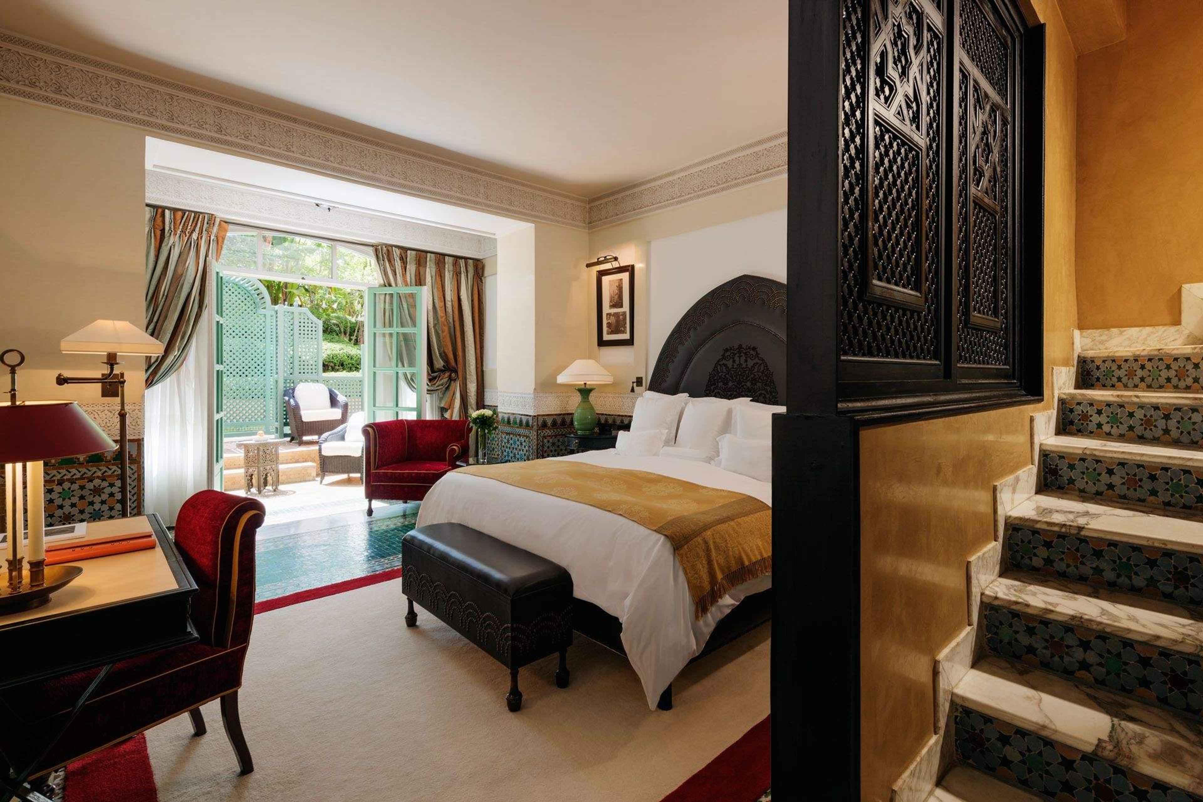 a suite bedroom opening directly onto a private plunge pool and terrace, seen past a carved black headboard and tiled staircase
