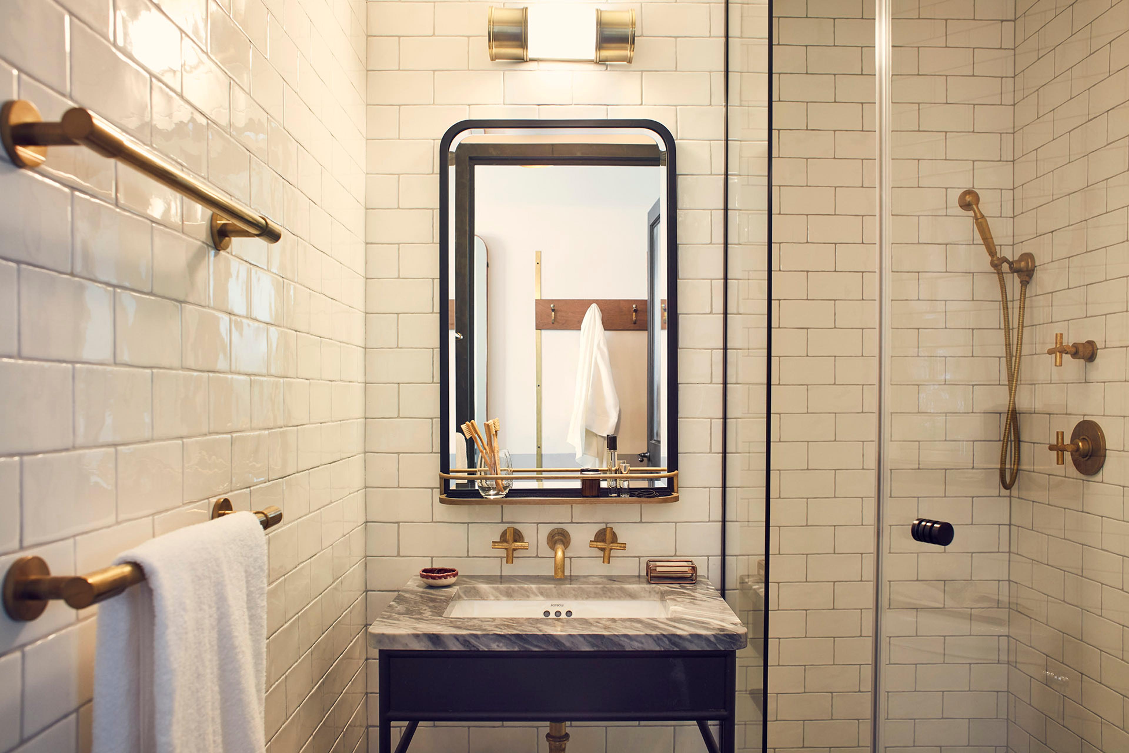 a bathroom with a marble-topped sink, a brass grab bar and towel rail, and a mirror reflecting a white robe hanging on a hook