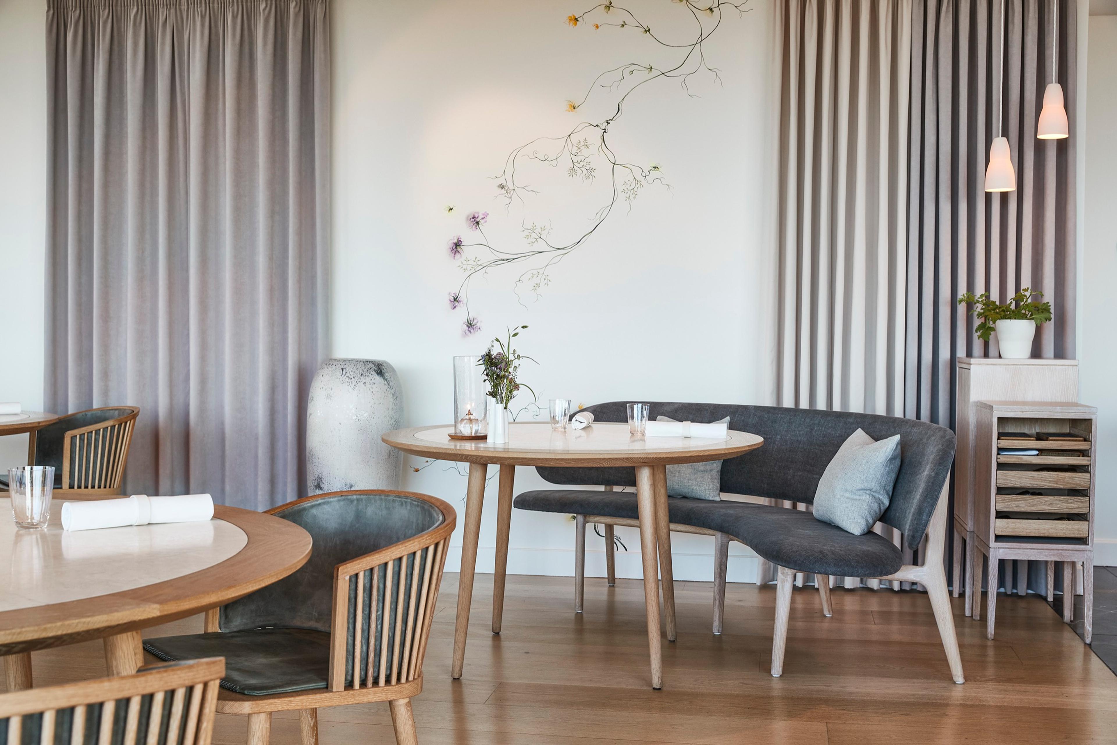 Geranium's dining room, a round table and grey armchairs beside tall curtained windows
