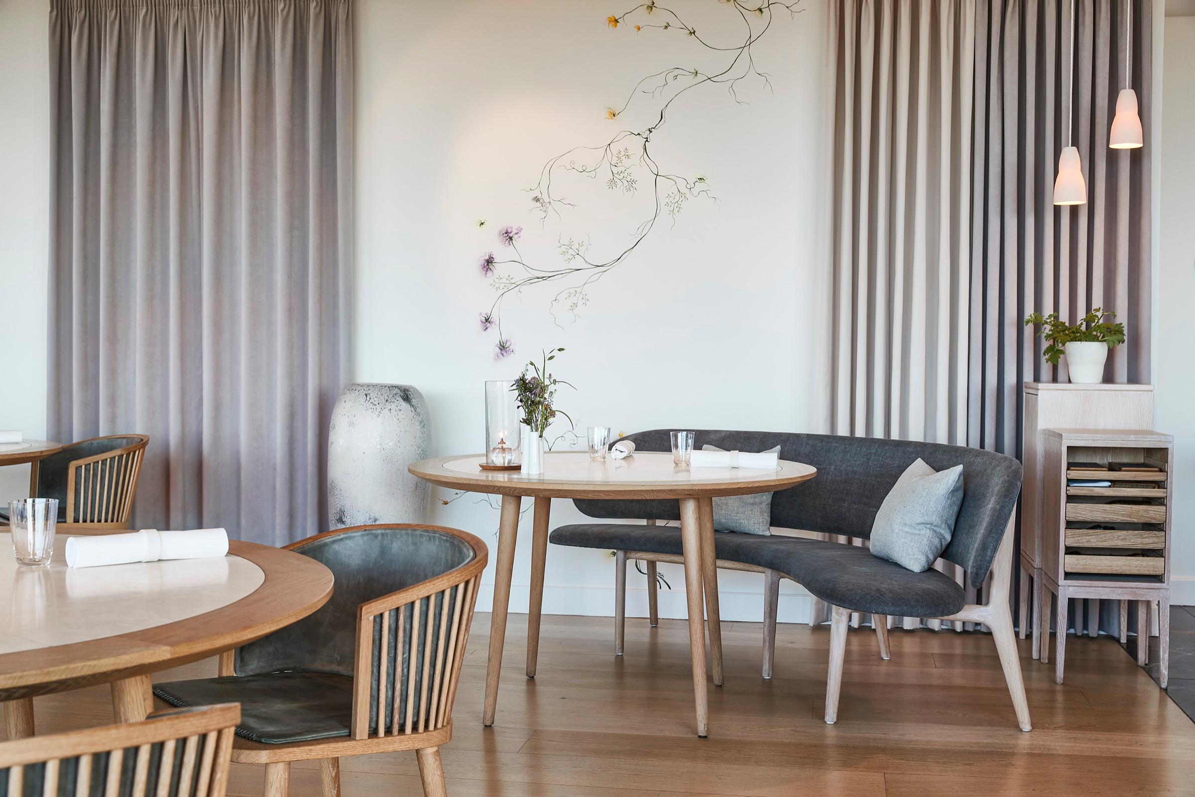 Geranium's dining room, a round table and grey armchairs beside tall curtained windows