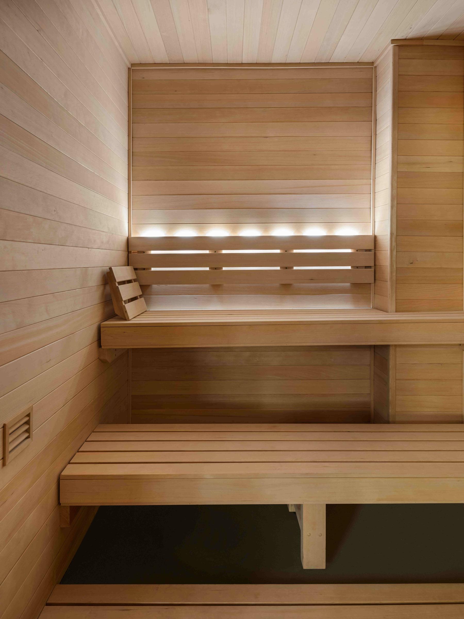 An empty cedar sauna with two tiered wooden benches and a row of small lights along the back wall.
