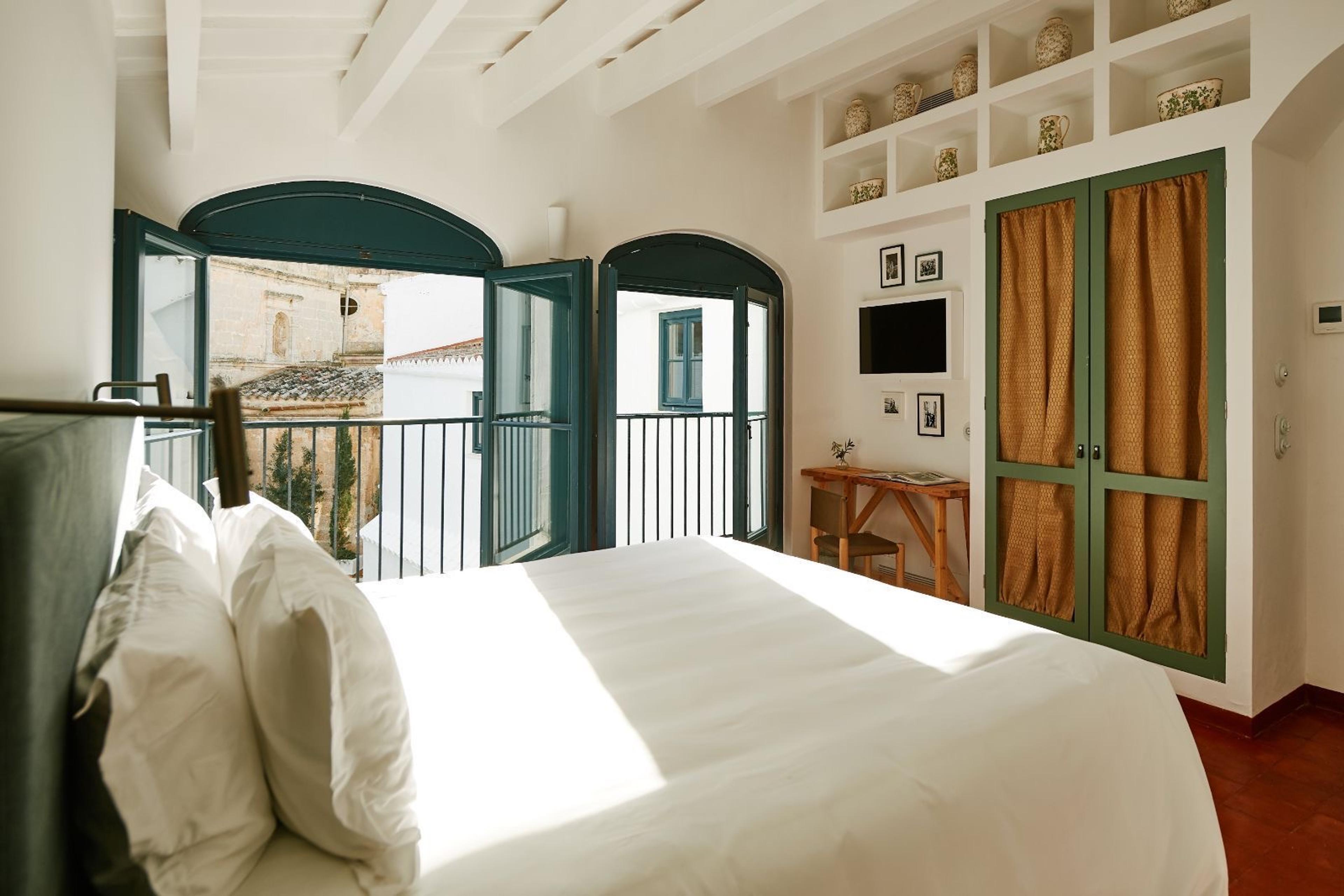 A bed facing two open glazed doors onto a balcony, with a stone church tower visible beyond the railings.