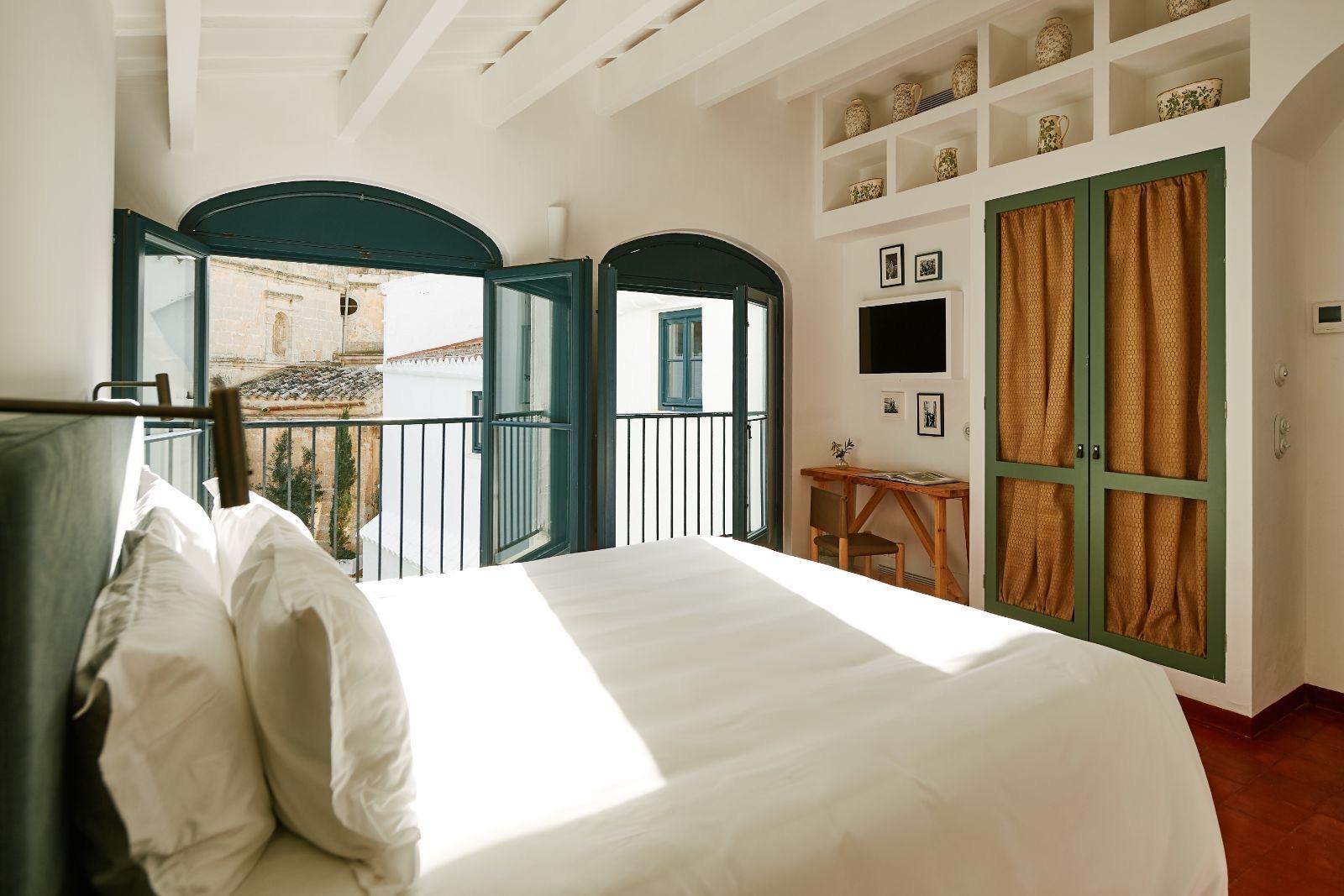 A bed facing two open glazed doors onto a balcony, with a stone church tower visible beyond the railings.