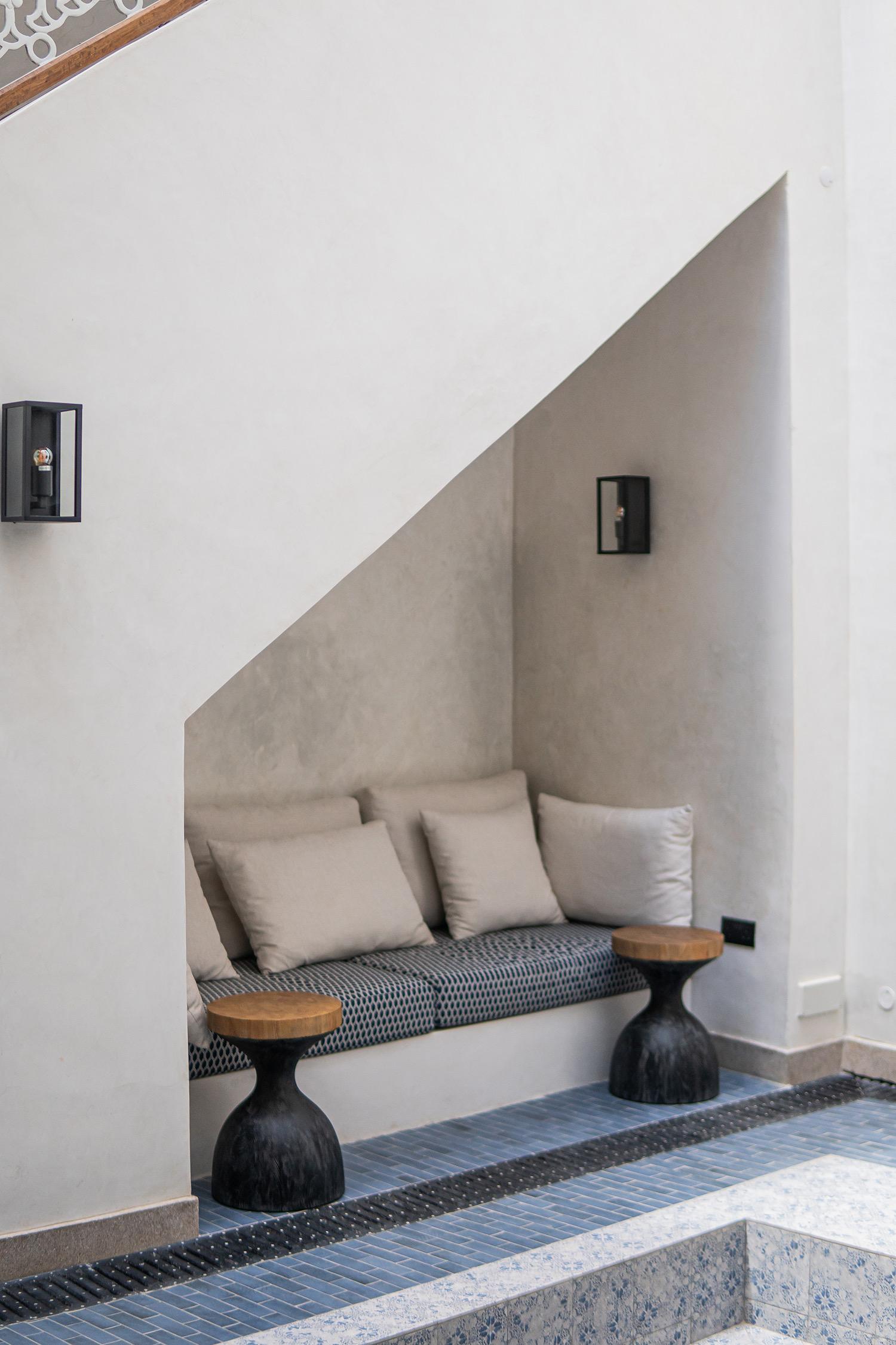 A built-in bench seat with grey cushions sits in a whitewashed alcove above a step edged in blue mosaic tile.