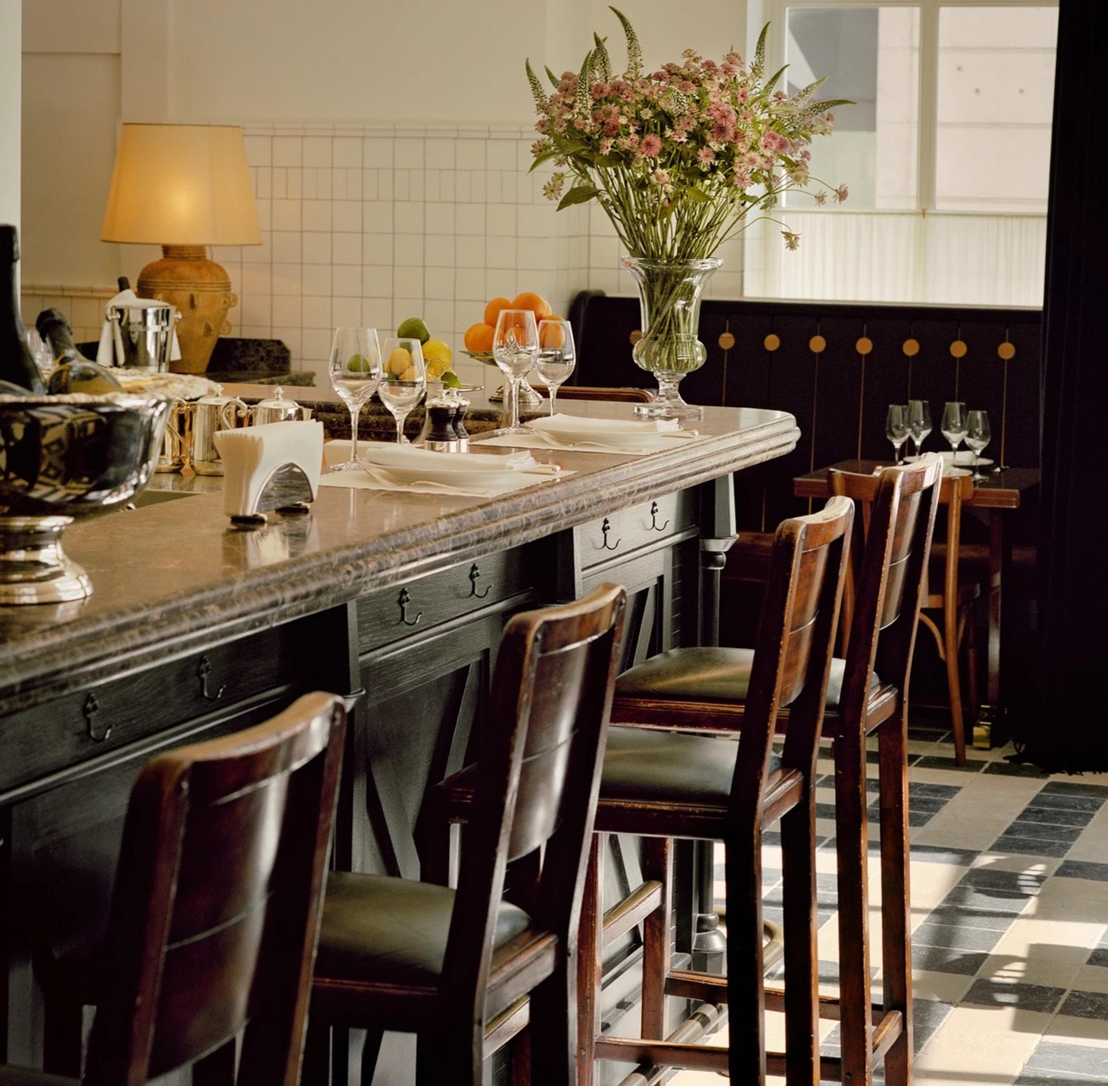 A narrow dining room with a counter of stools and banquette tables under white tiles and brass lamps.