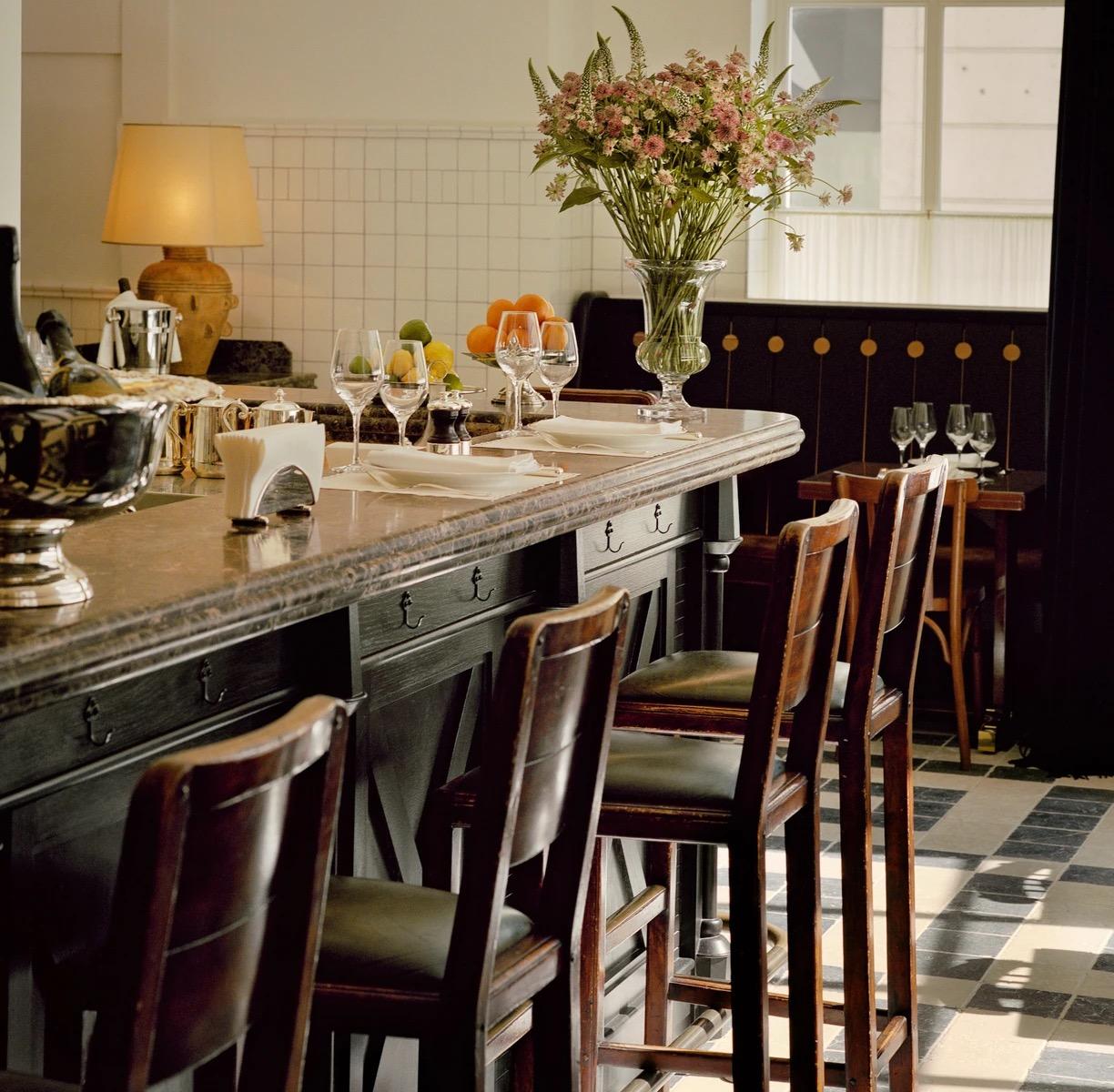 A narrow dining room with a counter of stools and banquette tables under white tiles and brass lamps.