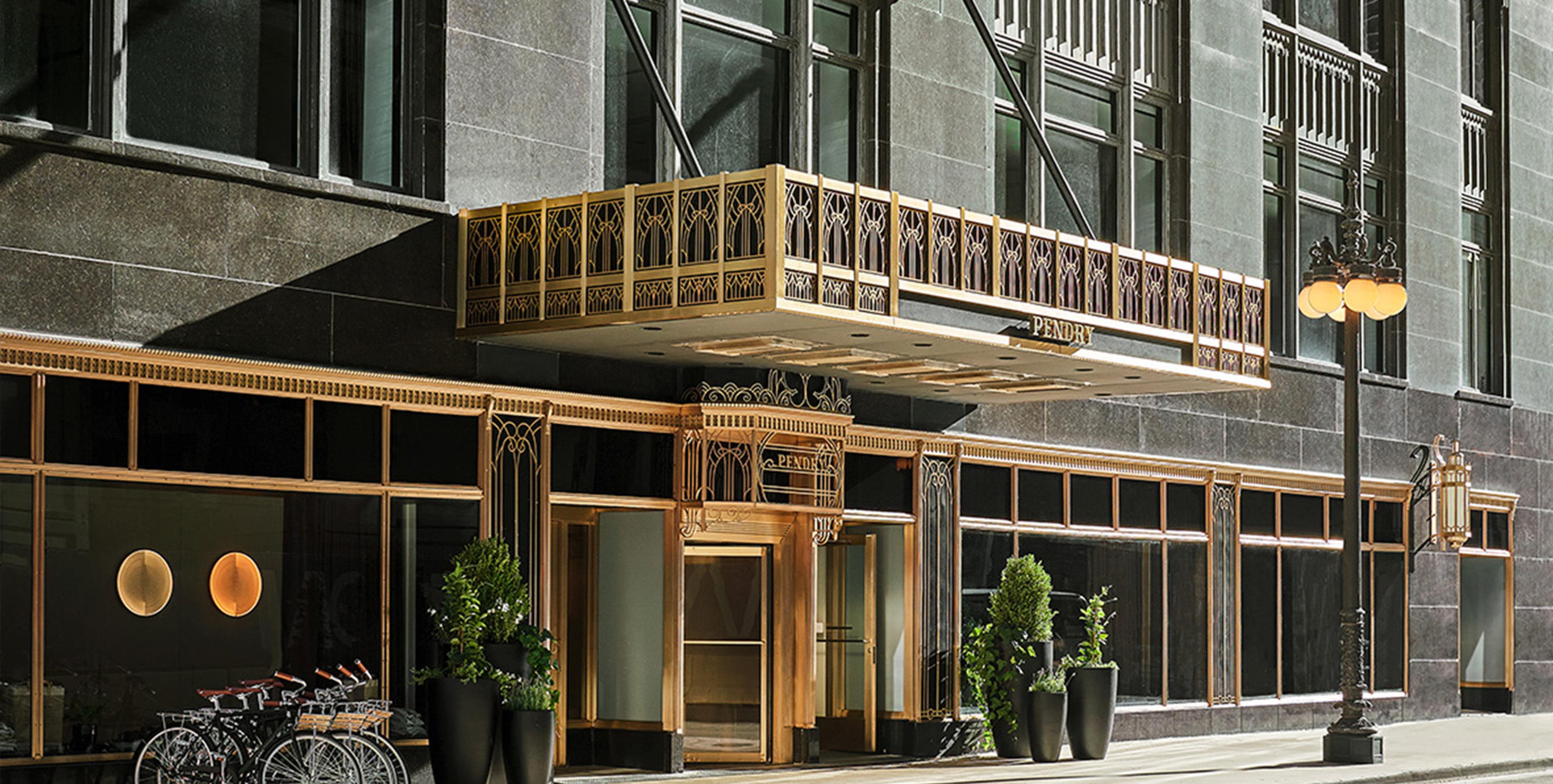 A close view of the hotel's gold Art Deco entrance canopy and ironwork, with bicycles parked below and a street lamp beside the door.