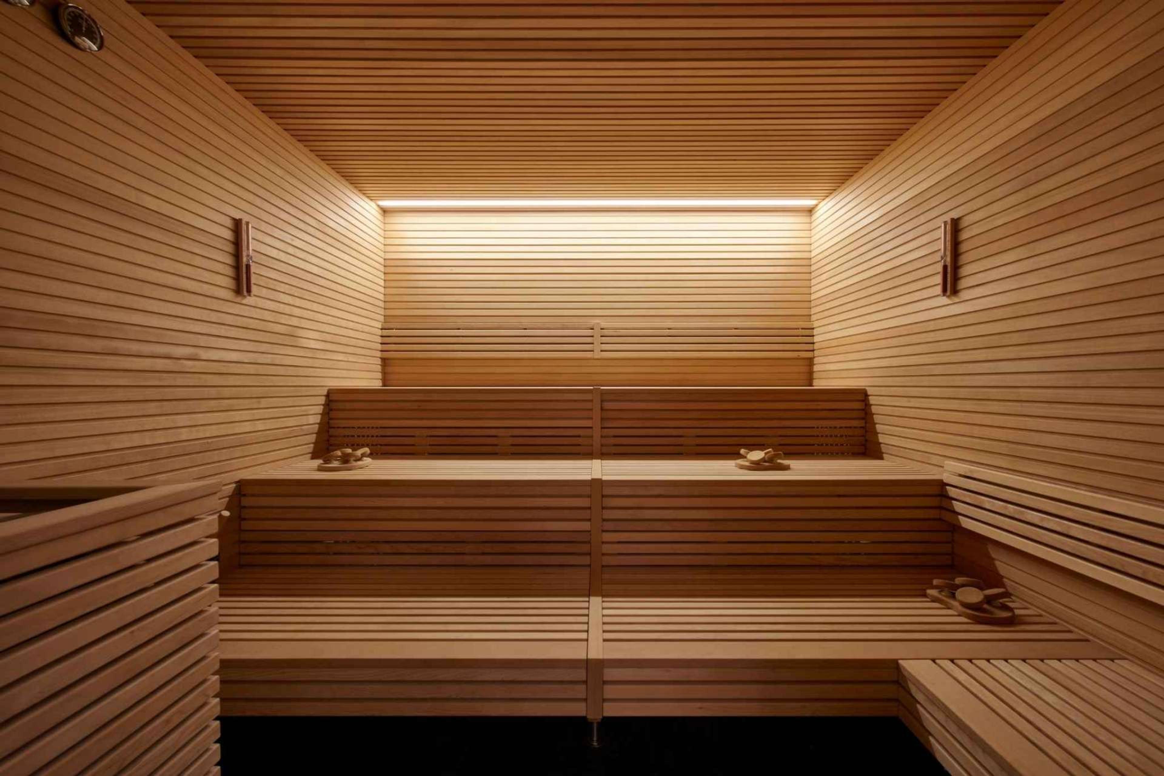 A wood-panelled sauna with two tiered benches and a lit panel at the far wall.