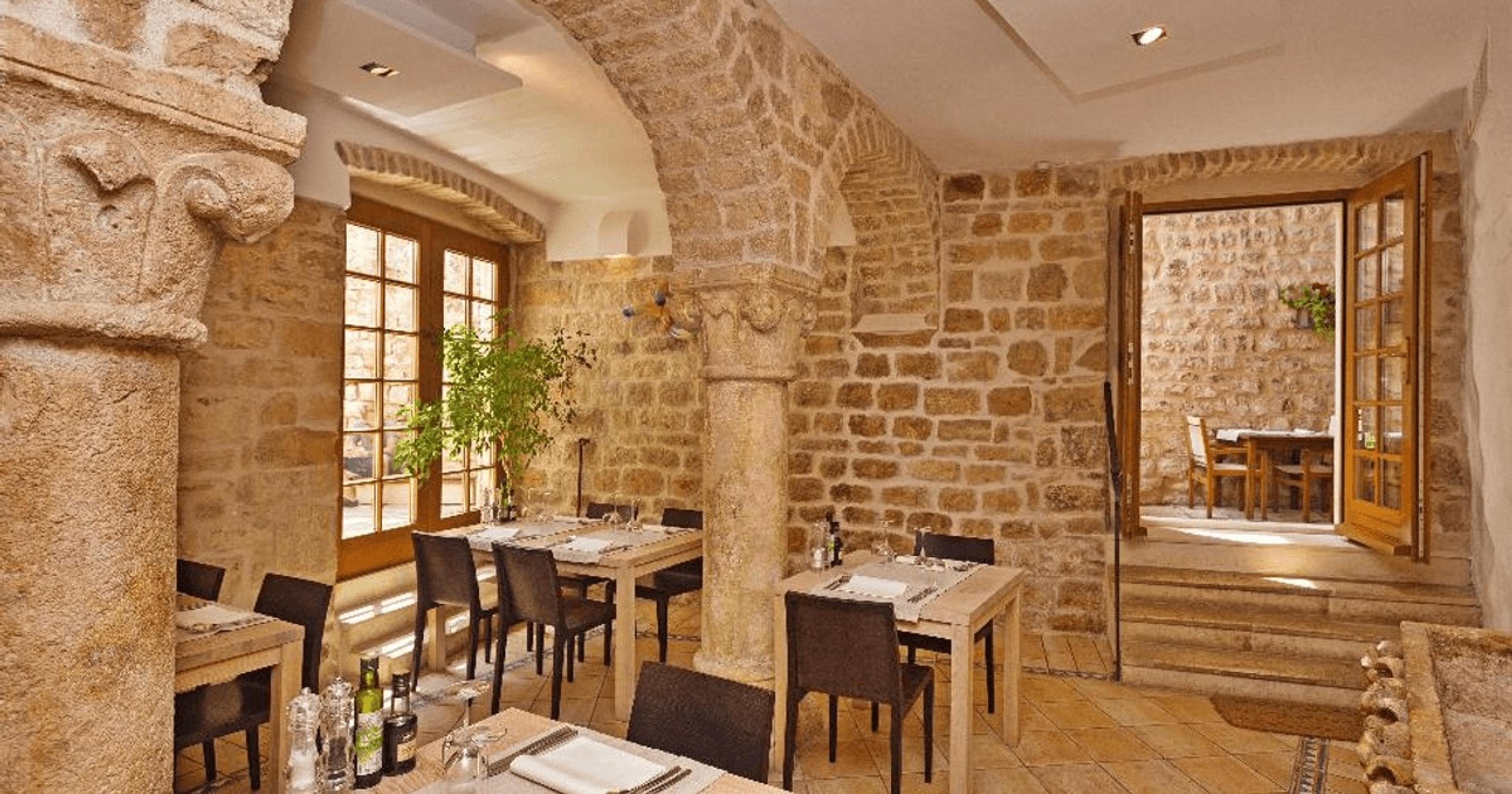 A dining room of bare stone walls and arched windows, tables laid for dinner