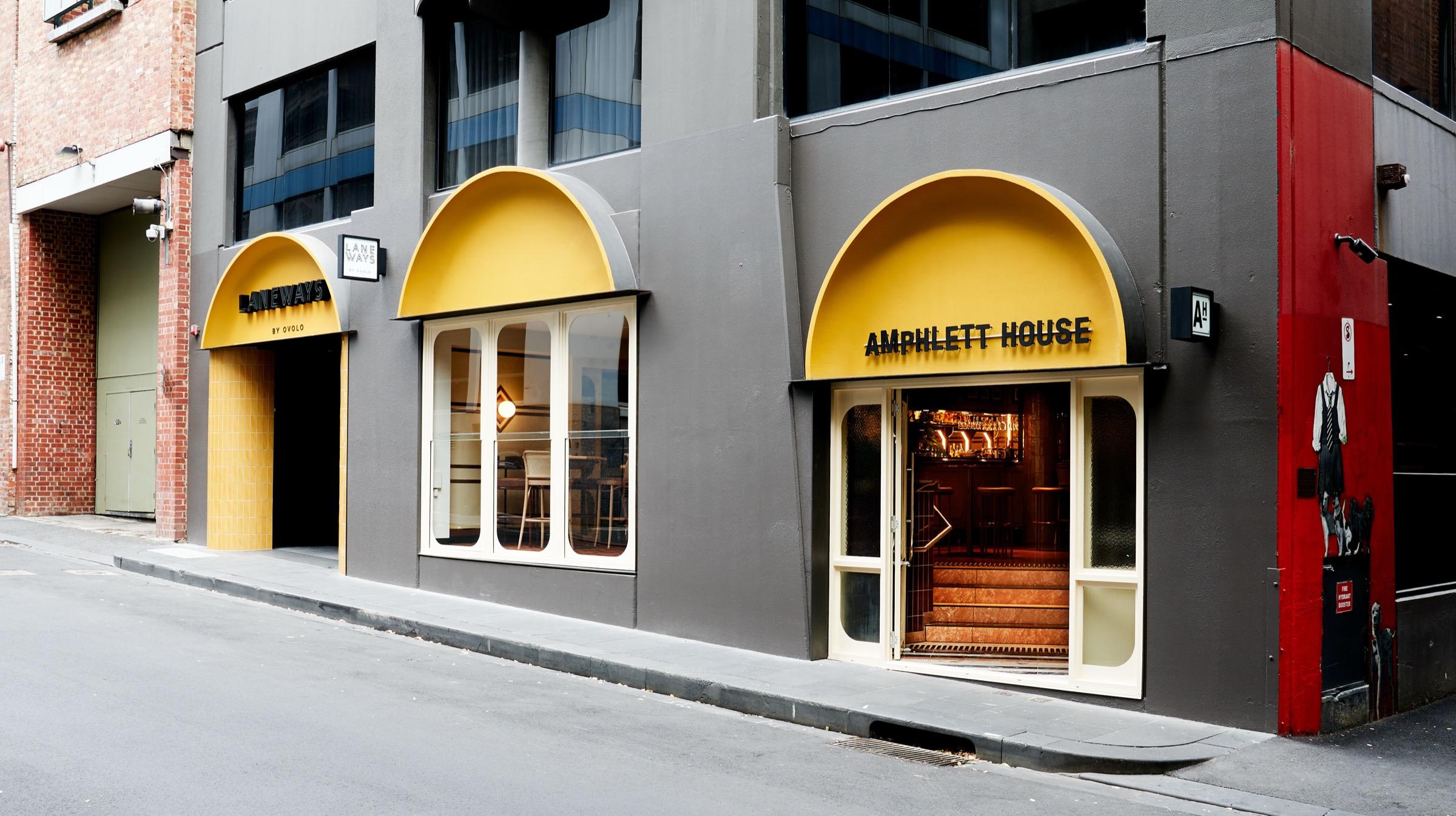 A laneway building facade with three yellow arched entrances, one marked Laneways and another Amphlett House, under a grey upper storey.