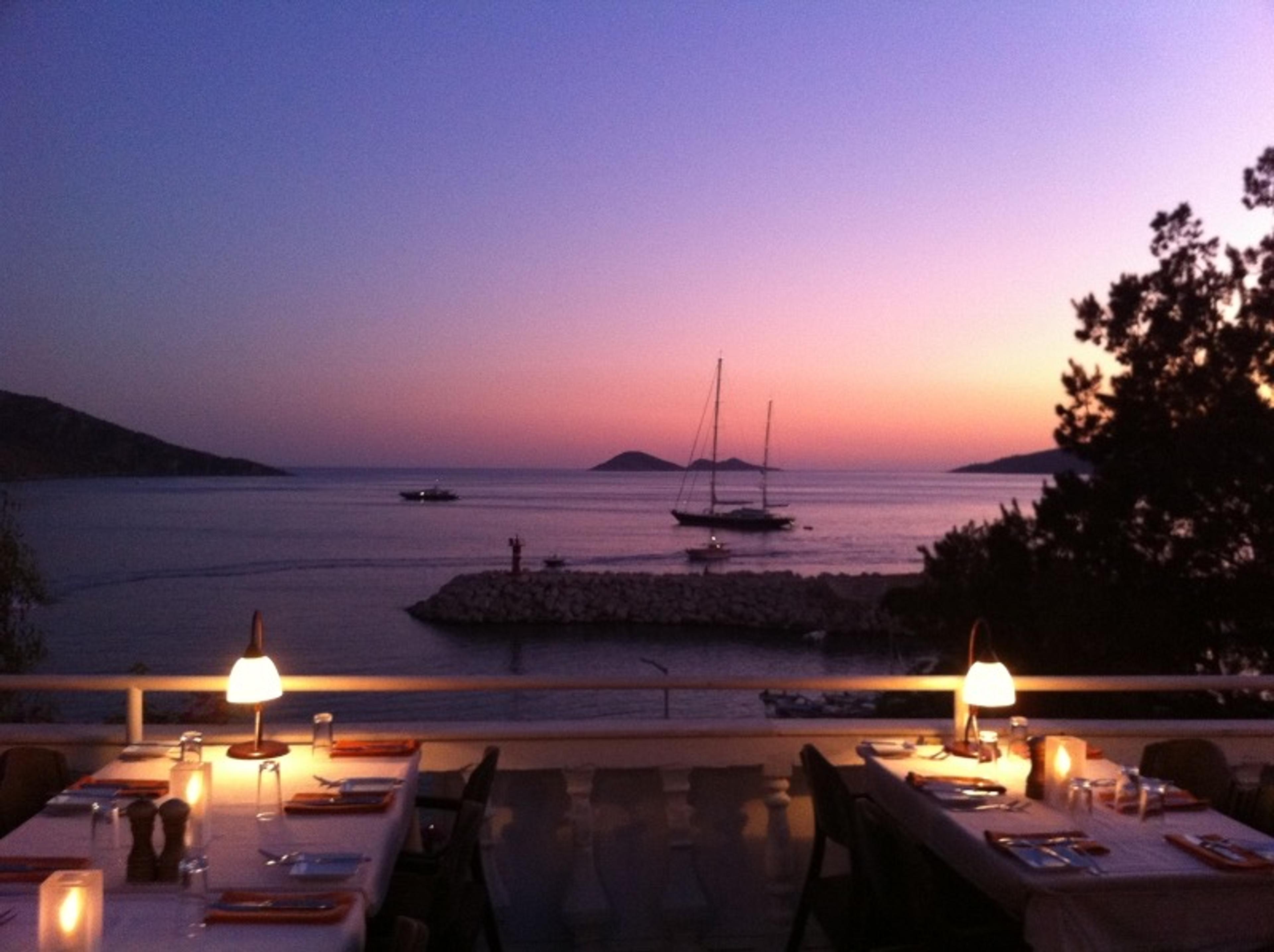 Tables lit for dinner on The Fish Terrace at dusk, Kalkan bay and moored boats beyond
