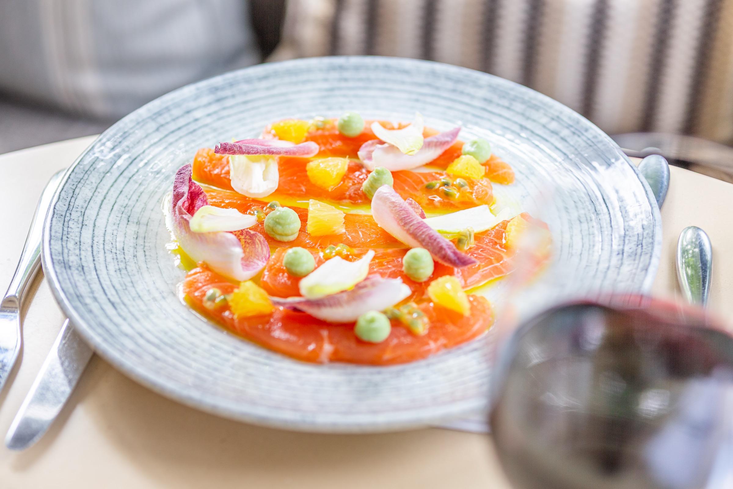 A plate of cured salmon with orange segments, pea puree and pickled red onion petals.