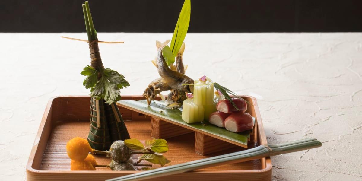 A seasonal dish arranged on a wooden tray with a sprig of bamboo