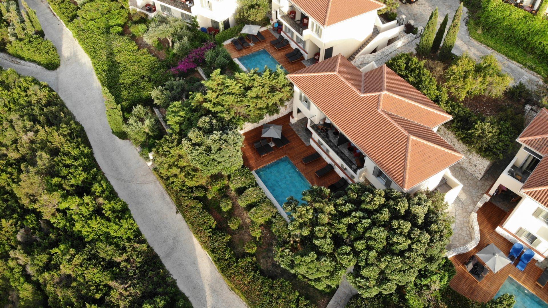 An overhead view of villas with private plunge pools and wooden terraces, set among trees beside a path.