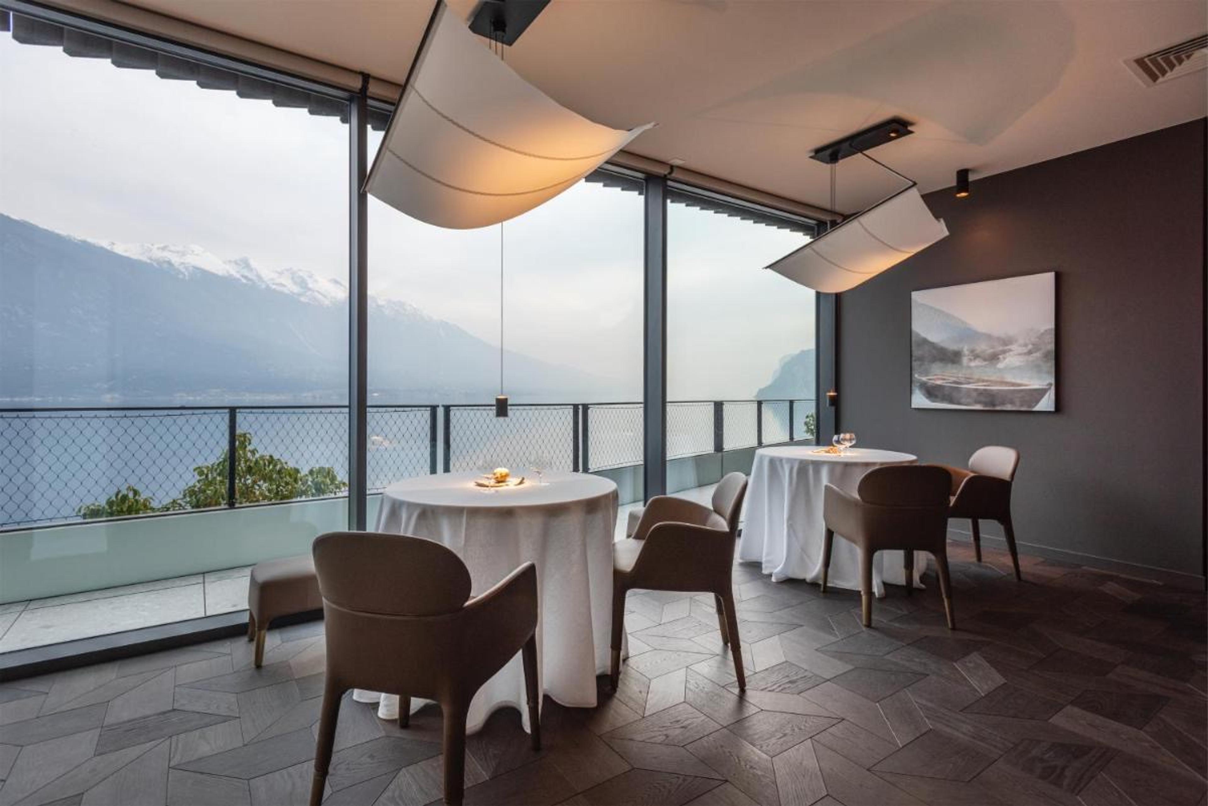 Round tables in white beside a wall of glass, the lake and the mountains outside