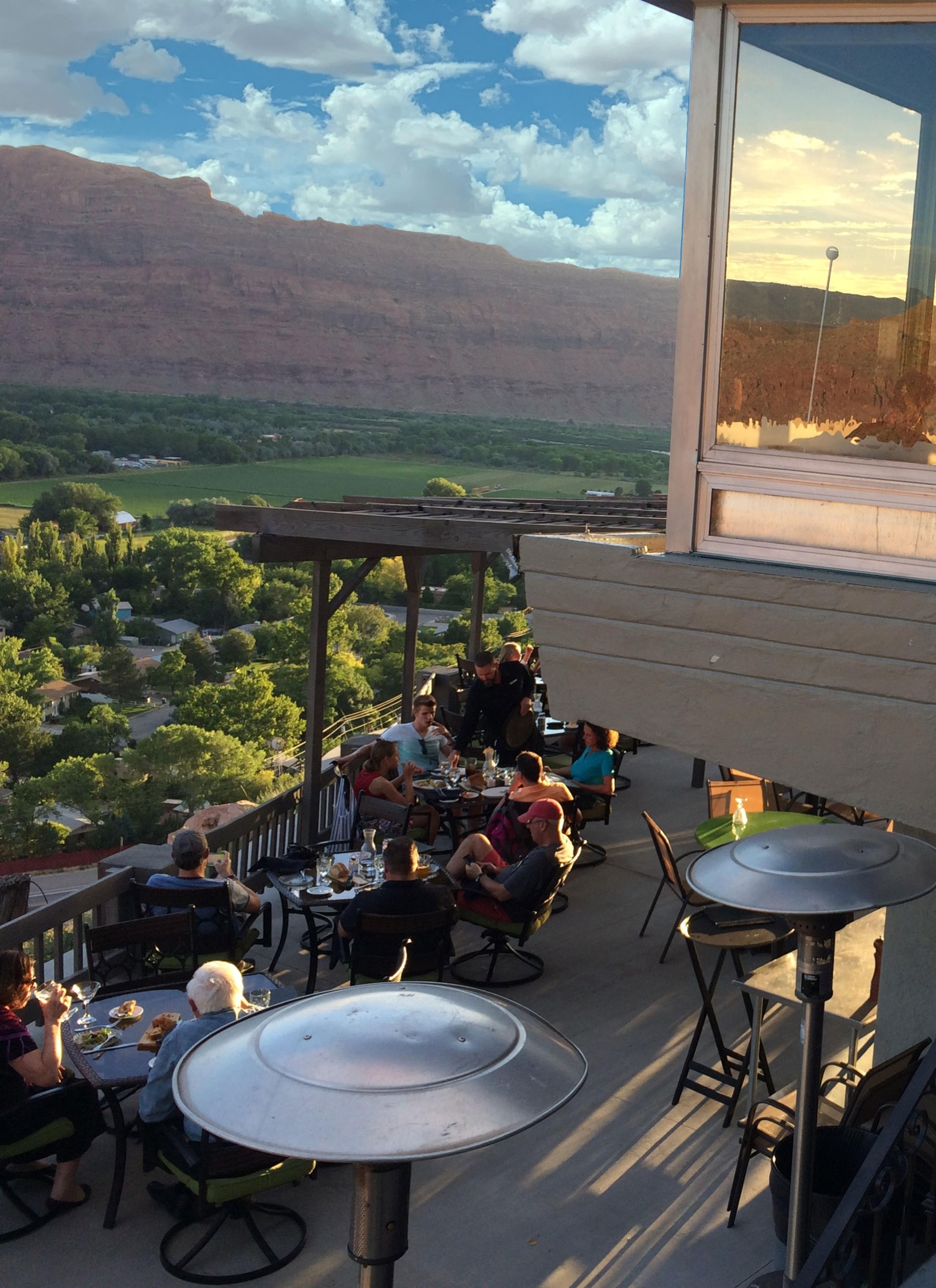 Diners on a deck high above Moab, the valley green below and the cliffs beyond