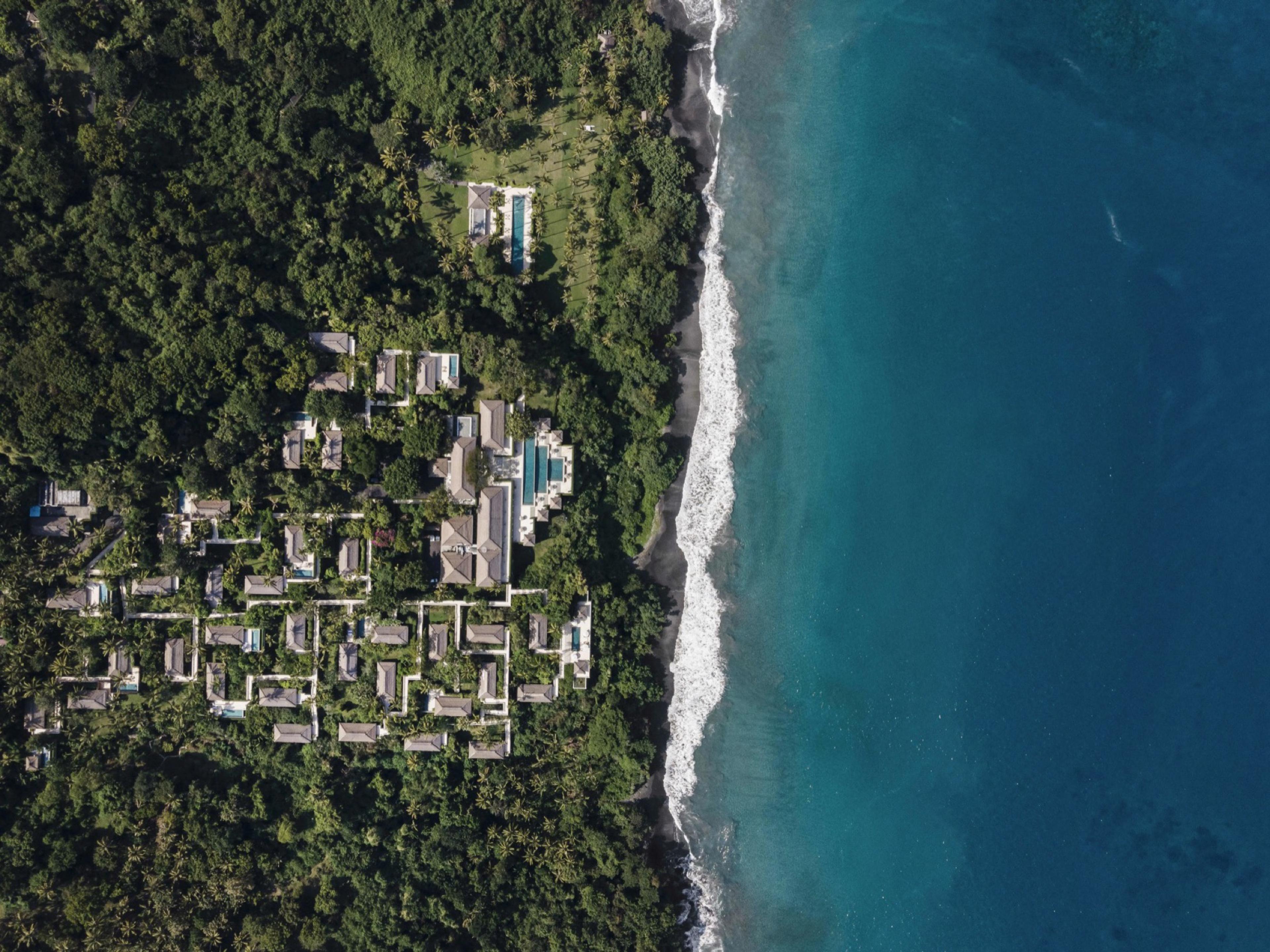 Amankila's thatched pavilions and pools from the air, in the forest above a black-sand shore on Bali's east coast