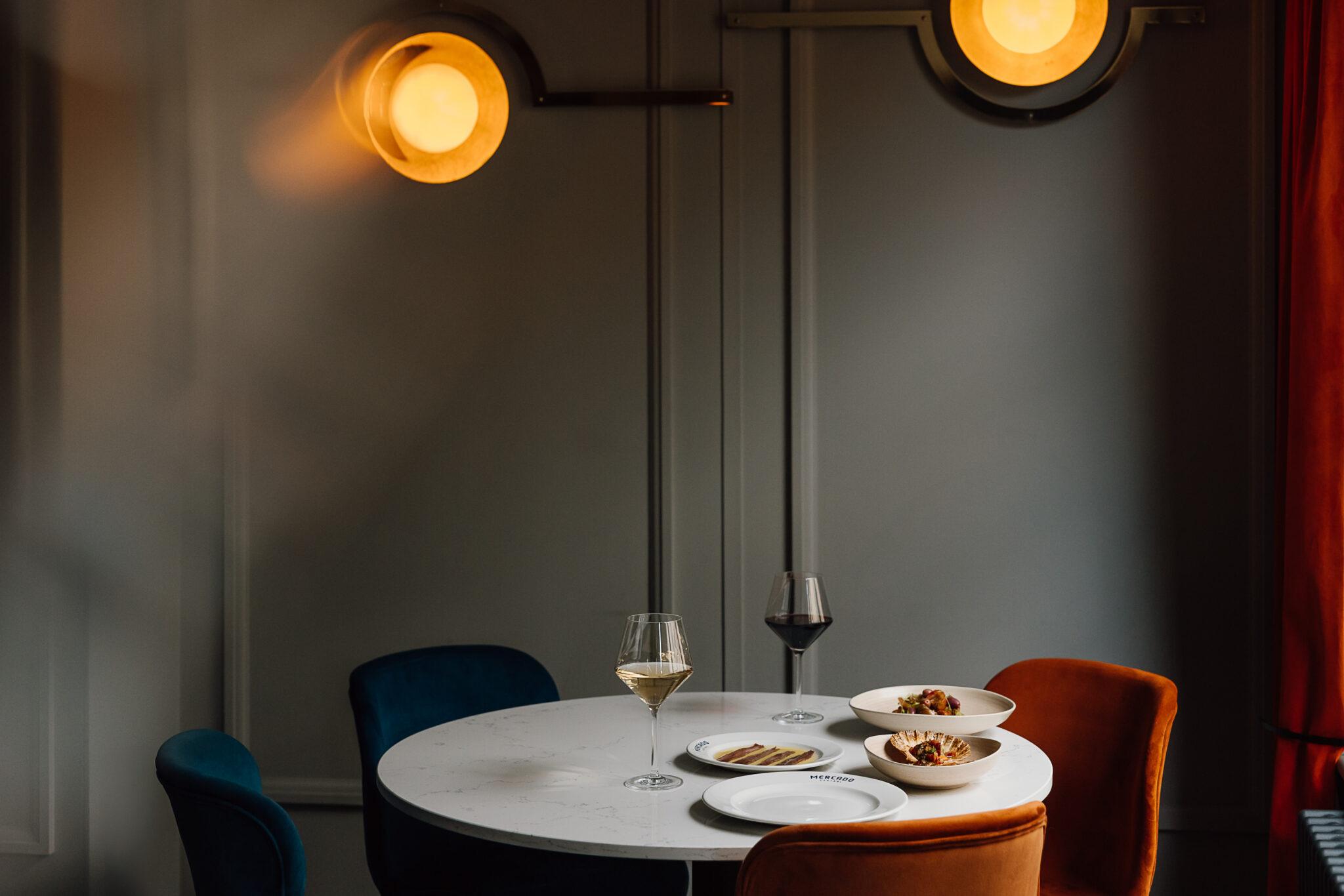 A round table laid for dinner under warm wall lights