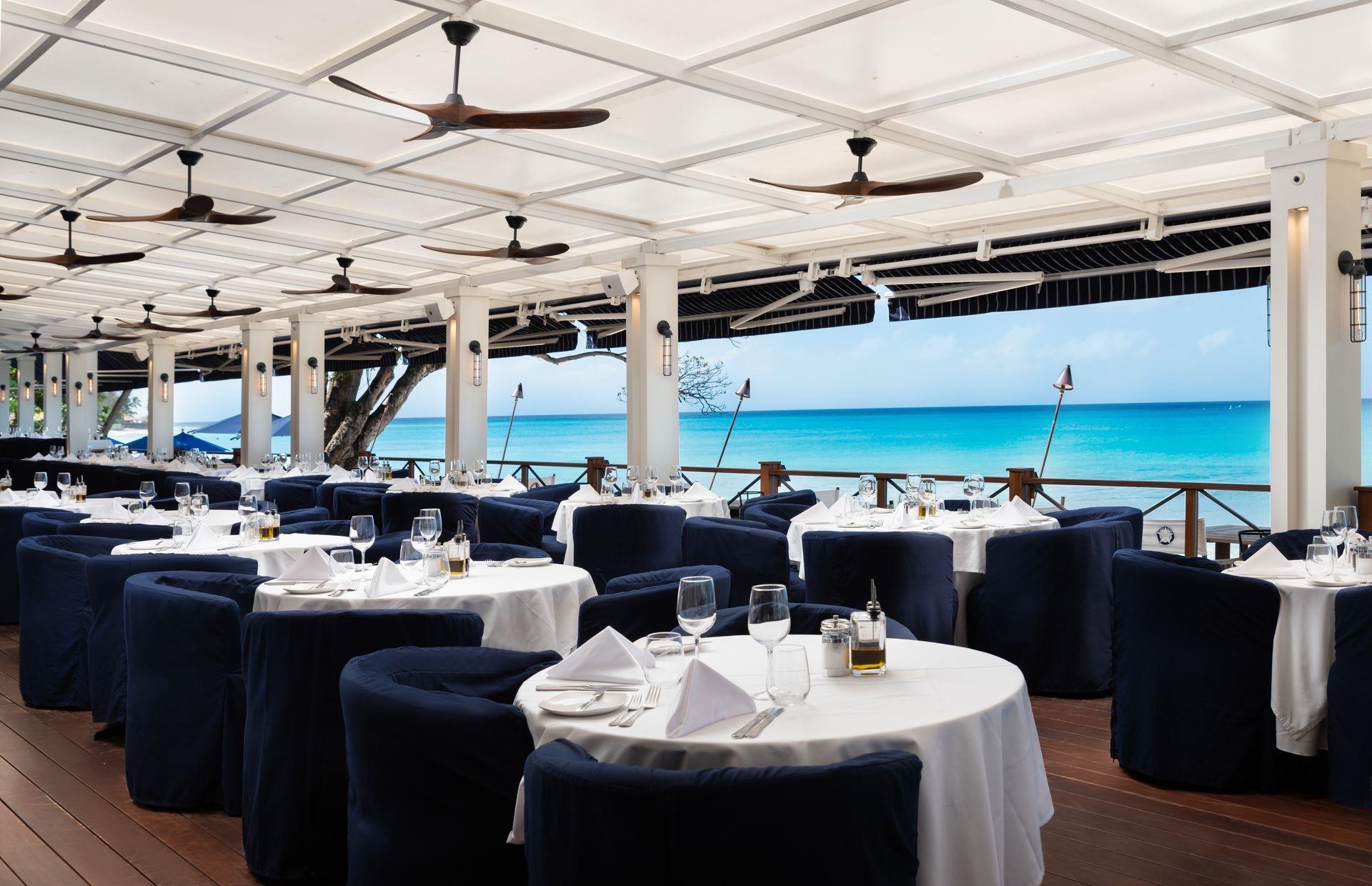 Tables laid on a covered terrace above the beach, the sea beyond