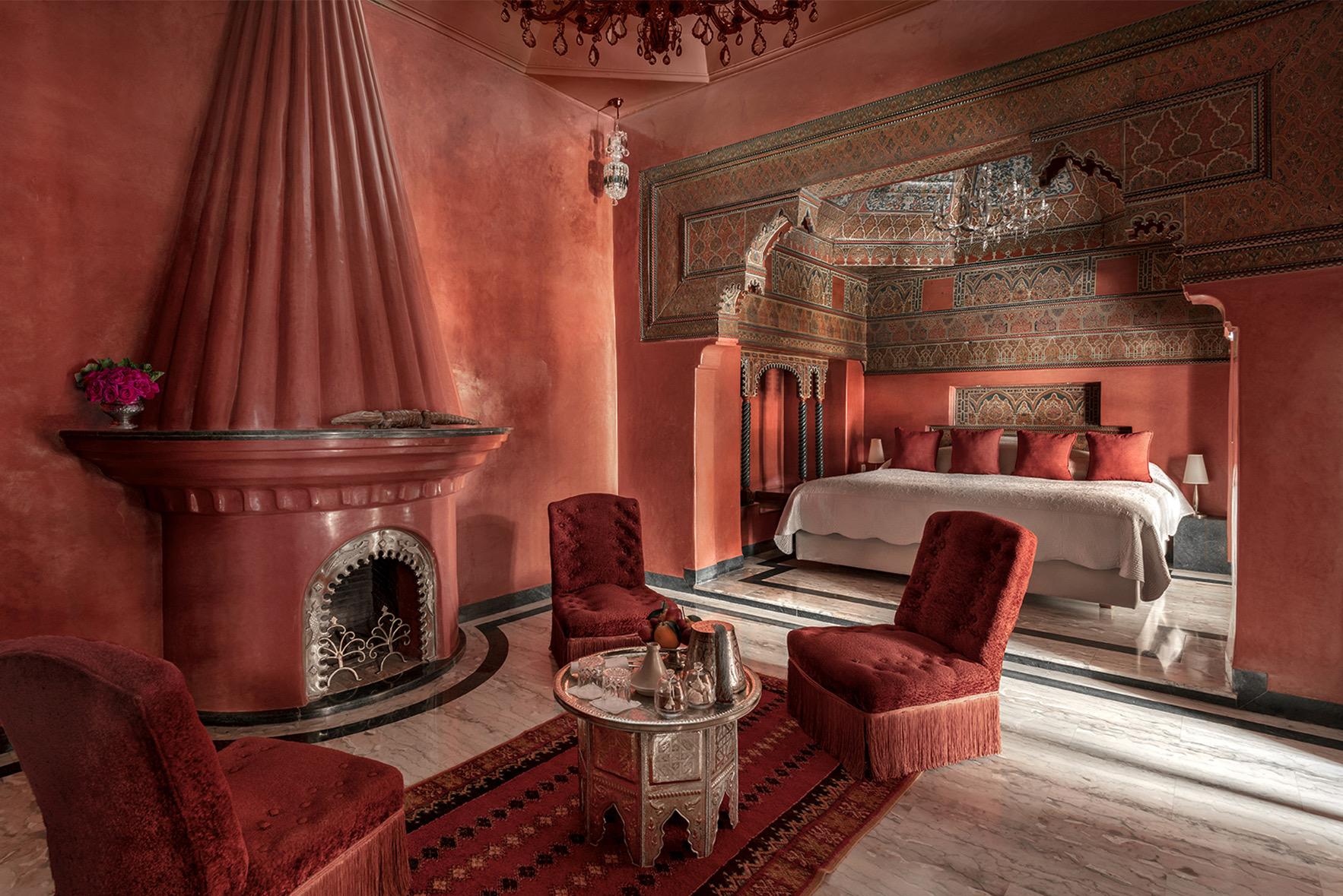 A terracotta suite with a round tented fireplace, velvet armchairs, a patterned rug, and a carved alcove bed beyond.