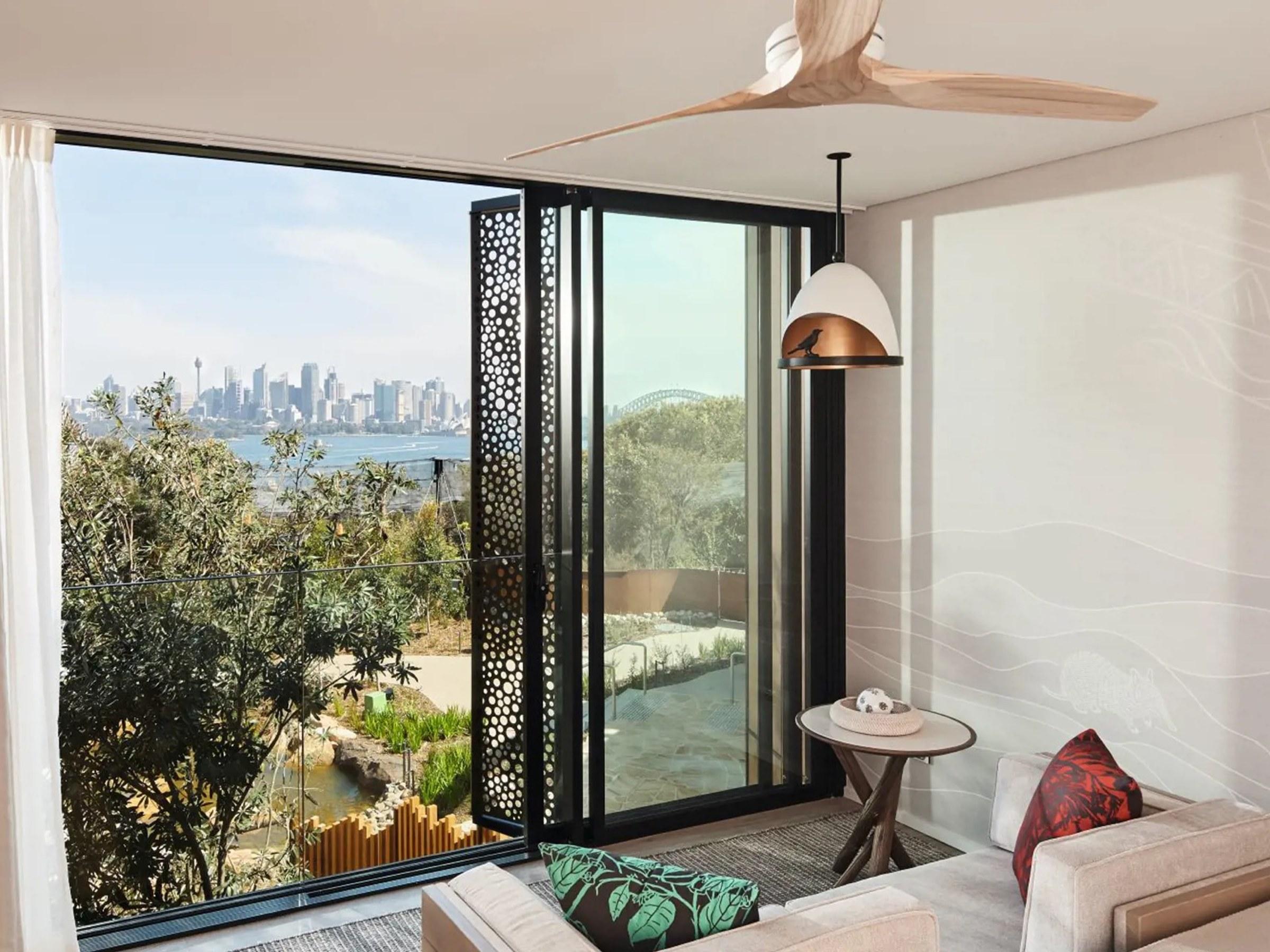 The city skyline and the Harbour Bridge across the water, seen through open doors from a room above the harbour's bushland