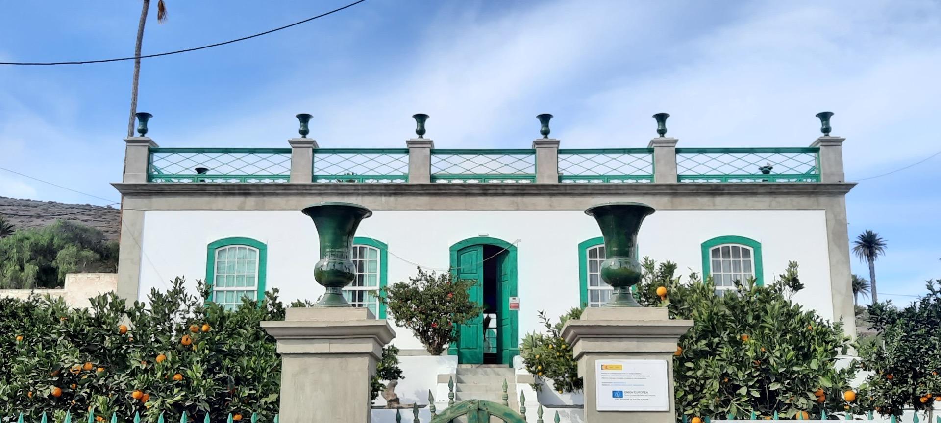 The hotel's white two-storey facade with green-shuttered windows and a central door, framed by orange trees and two green urns.