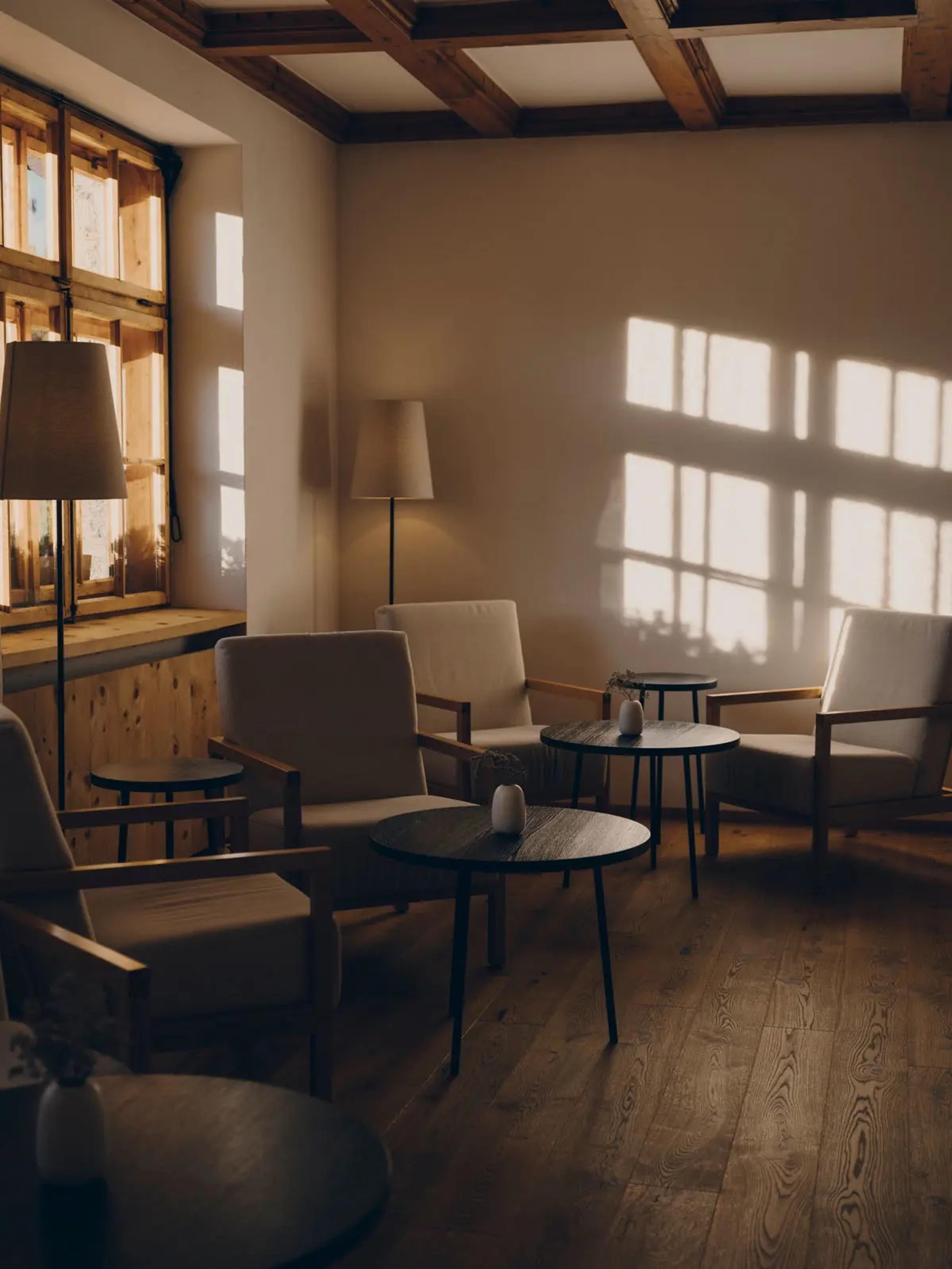 Armchairs and low tables sit in a timber-beamed lounge, with afternoon light falling through a window onto the wall.