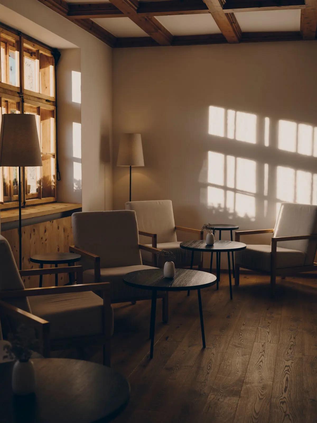 Armchairs and low tables sit in a timber-beamed lounge, with afternoon light falling through a window onto the wall.