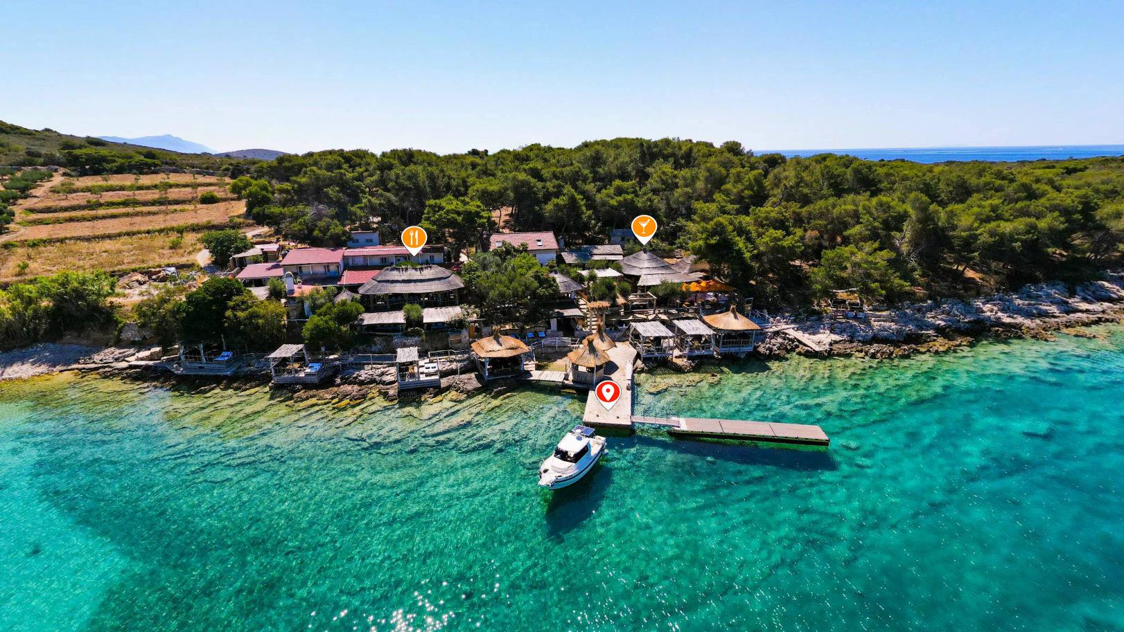A wooded island cove from the air, a jetty and boats on turquoise water