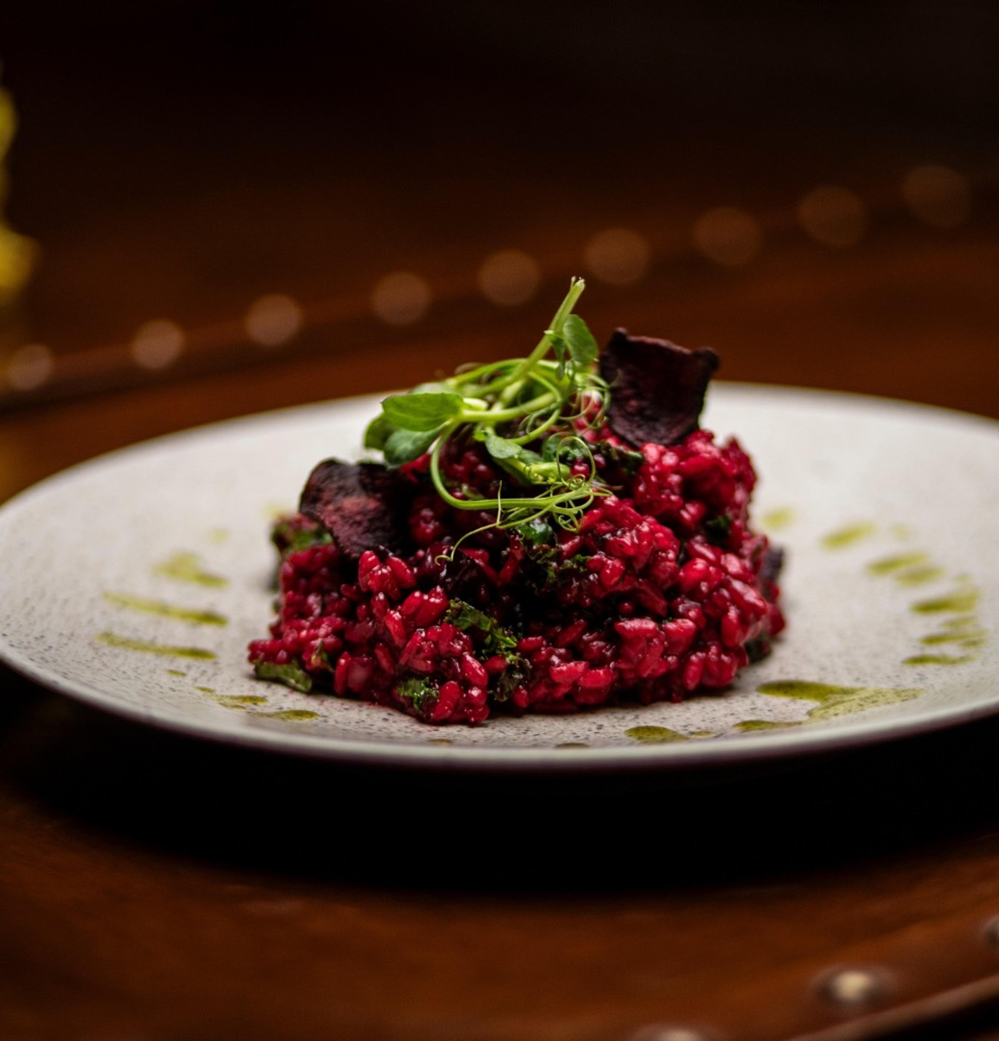A dish of beetroot and red grains topped with herbs, on a white plate against a dark background.