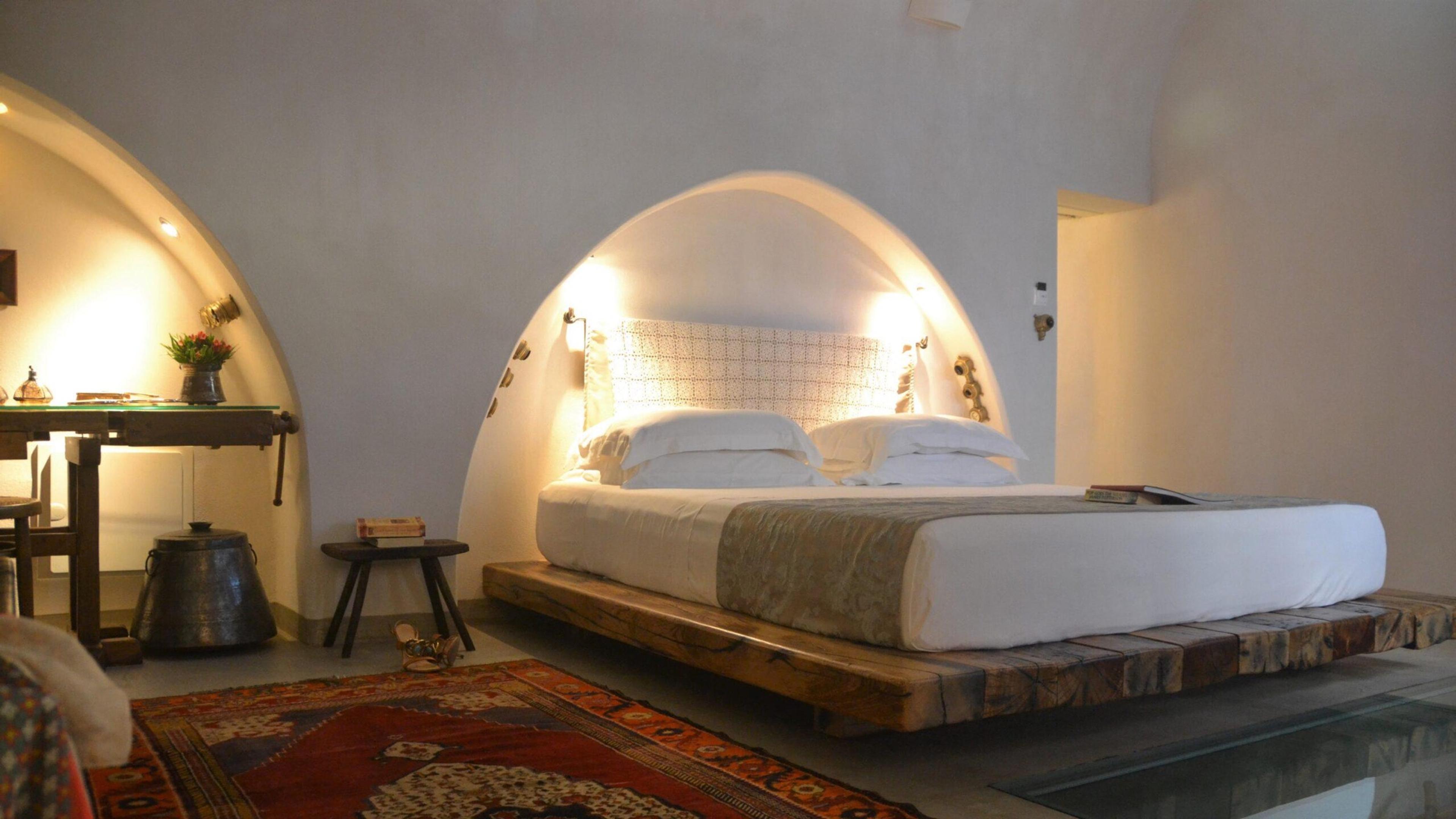 A bed set into a vaulted stone alcove, on a low wooden platform with a kilim rug in front.