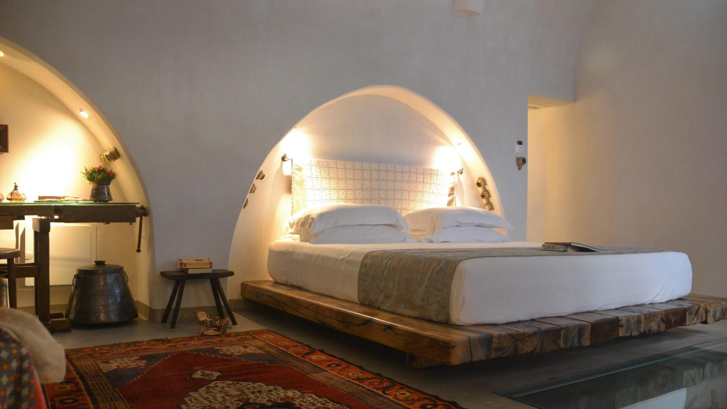 A bed set into a vaulted stone alcove, on a low wooden platform with a kilim rug in front.