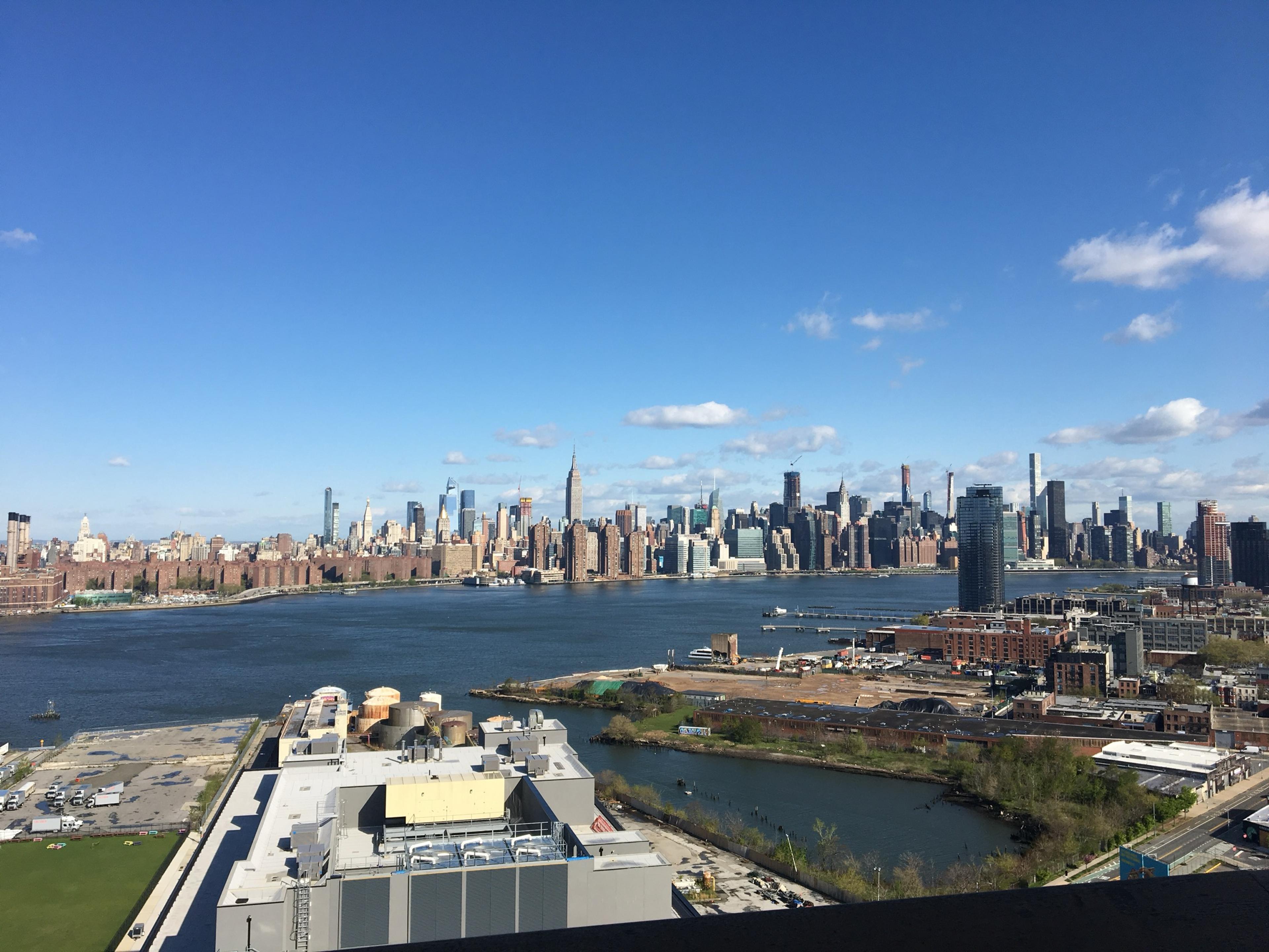 Midtown Manhattan across the East River from high above Williamsburg, the Empire State Building in the middle of the skyline under a bright spring sky