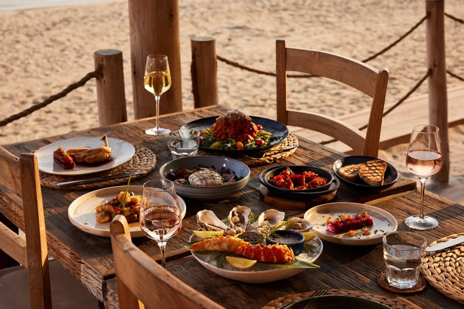 A table of dishes and wine set out on the sand at Laguna Beach Taverna
