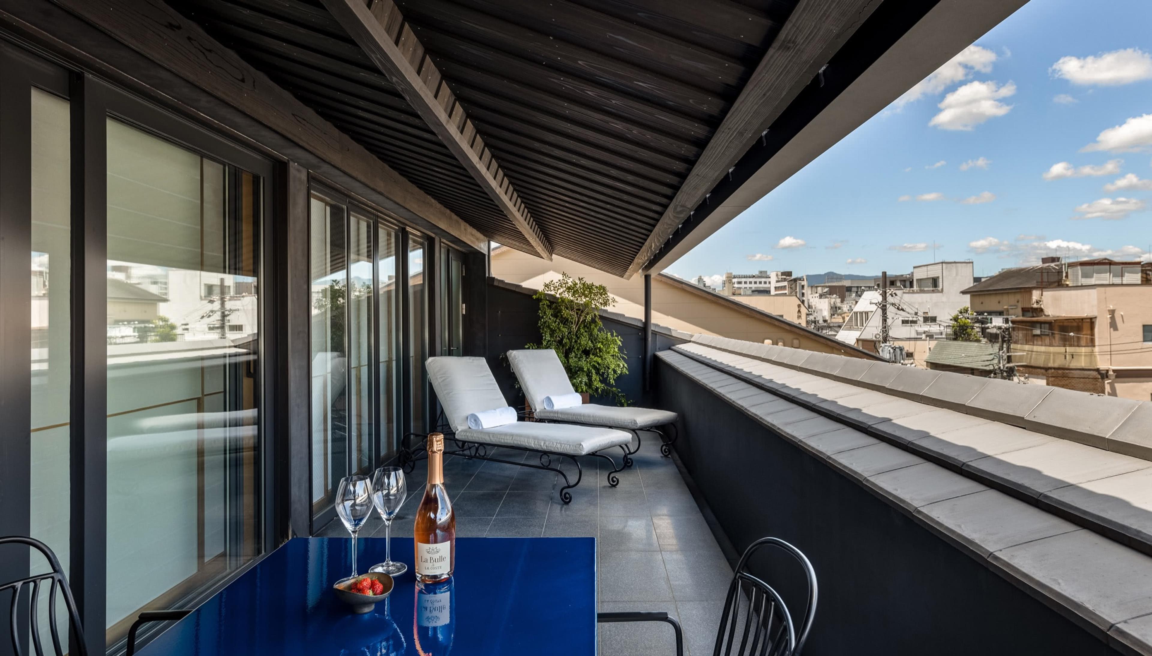 a rooftop terrace with two white loungers and a blue table set for champagne, under an open sky above the town's rooftops