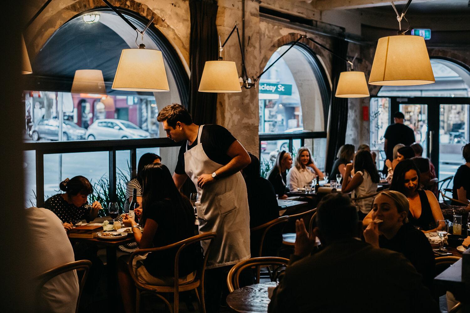 A busy dining room under arched windows and globe lamps