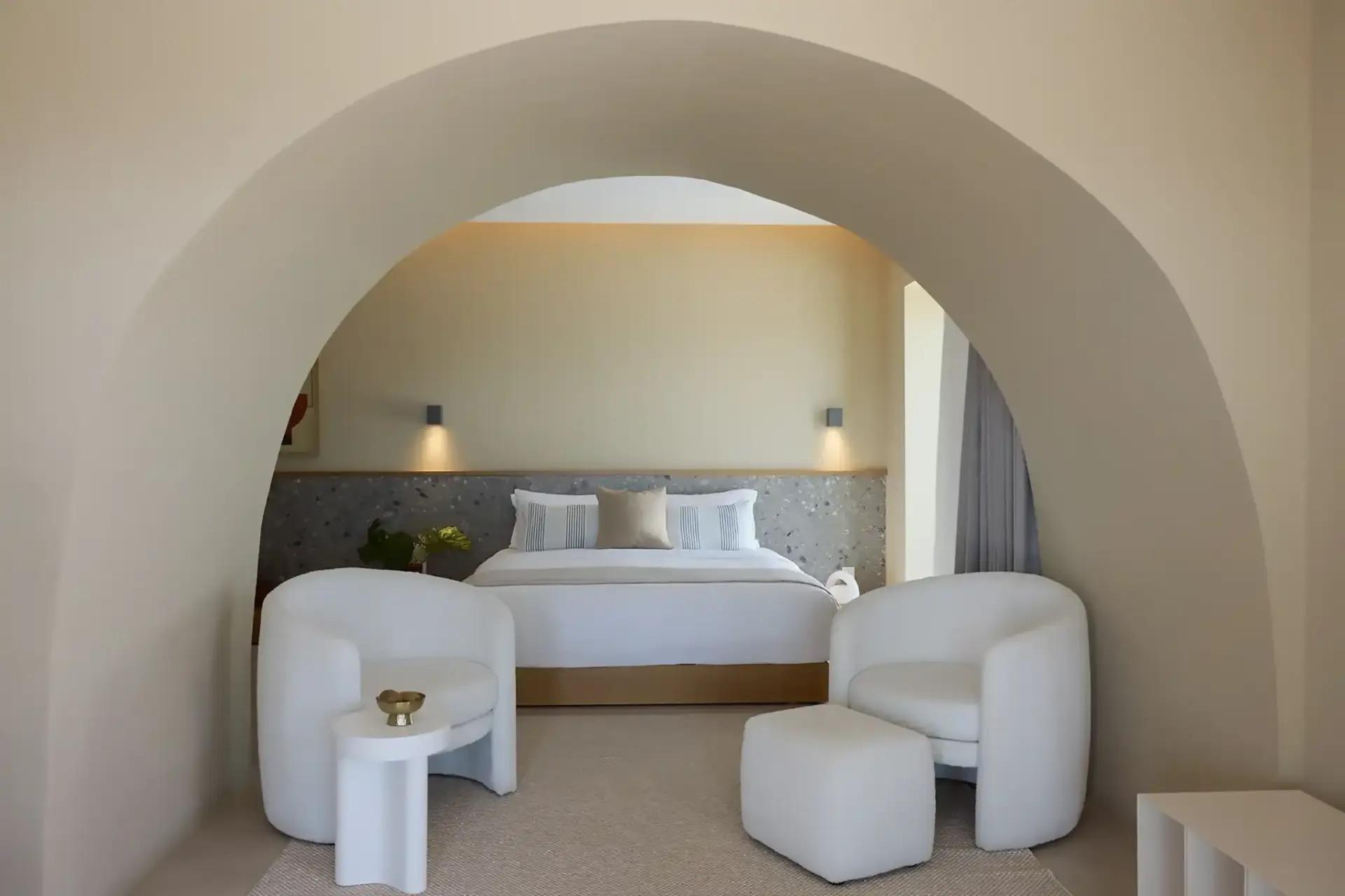 A bed and two armchairs seen through a deep plastered archway.