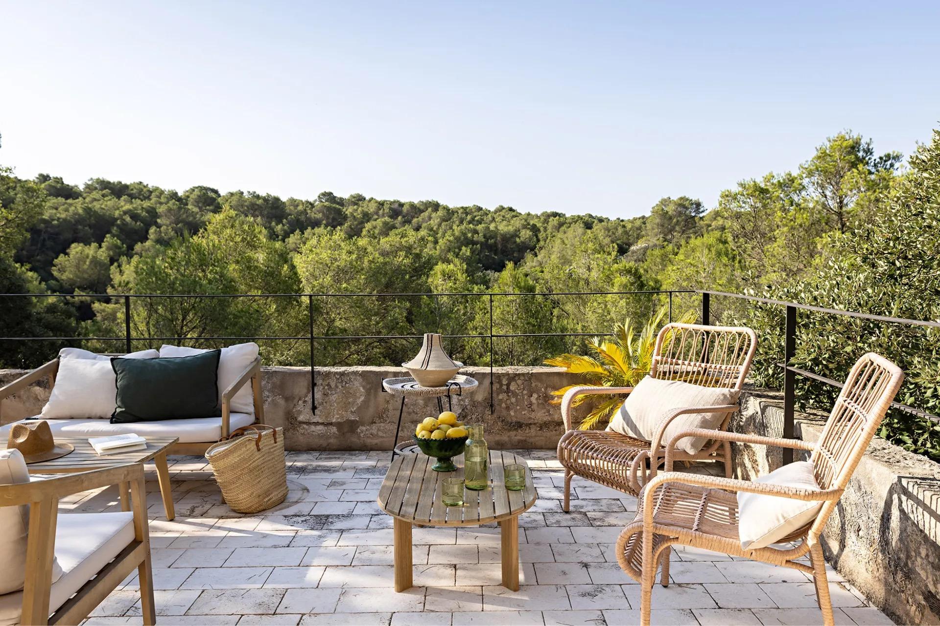 a stone roof terrace with woven rattan chairs and a wooden coffee table holding a bowl of lemons, overlooking wooded hills