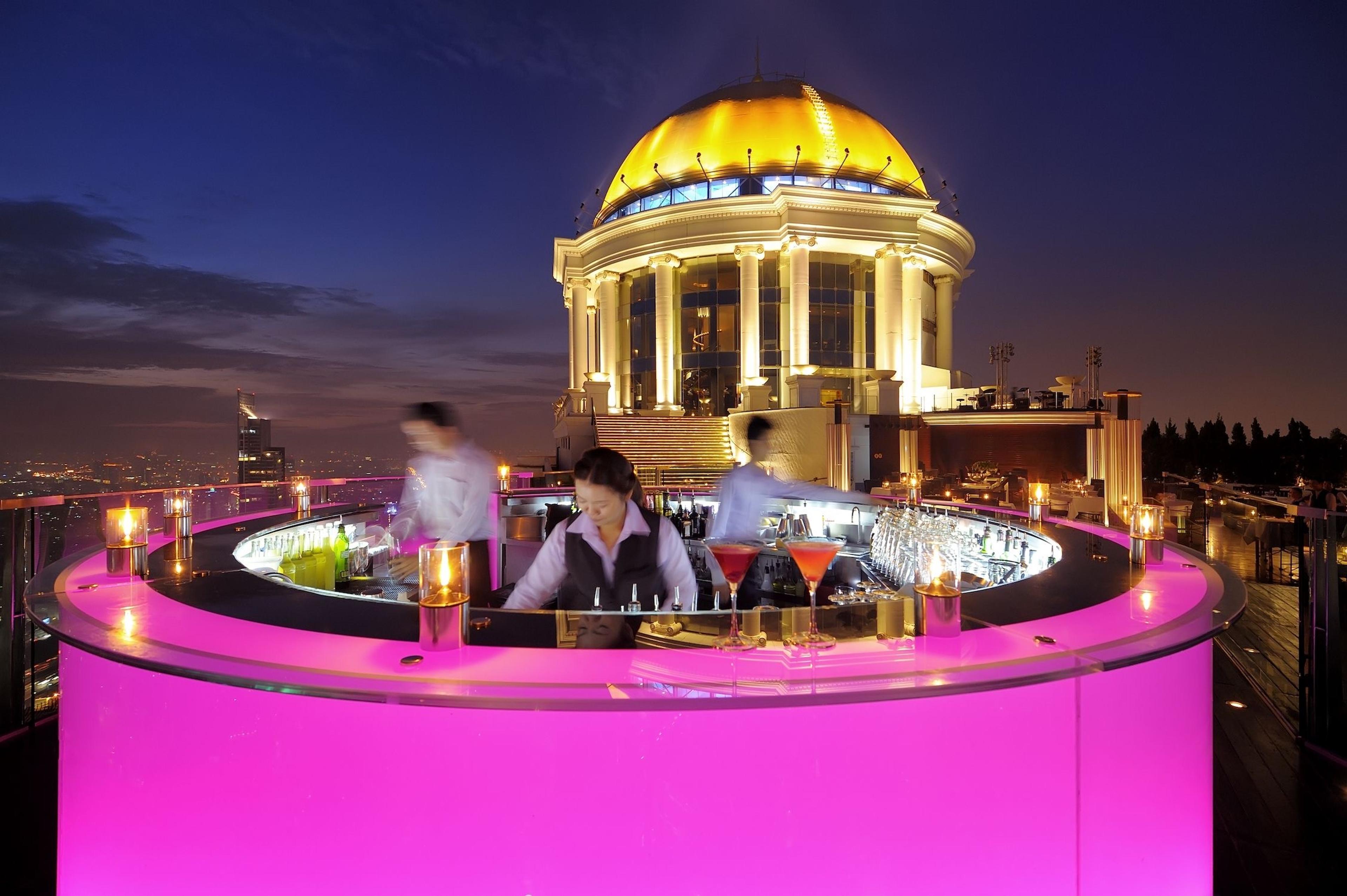 A circular bar lit pink beneath a gilded dome, high above Bangkok at dusk