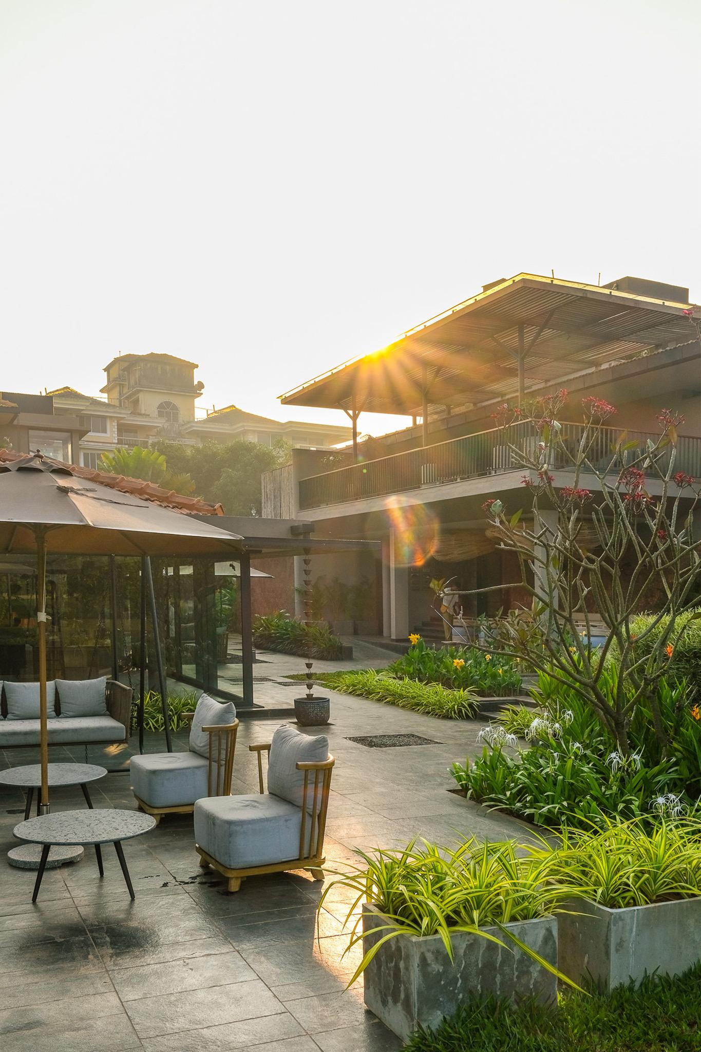 An outdoor lounge area with grey sofas and armchairs around low tables, the hotel's tiled roofline behind it lit by low sun.