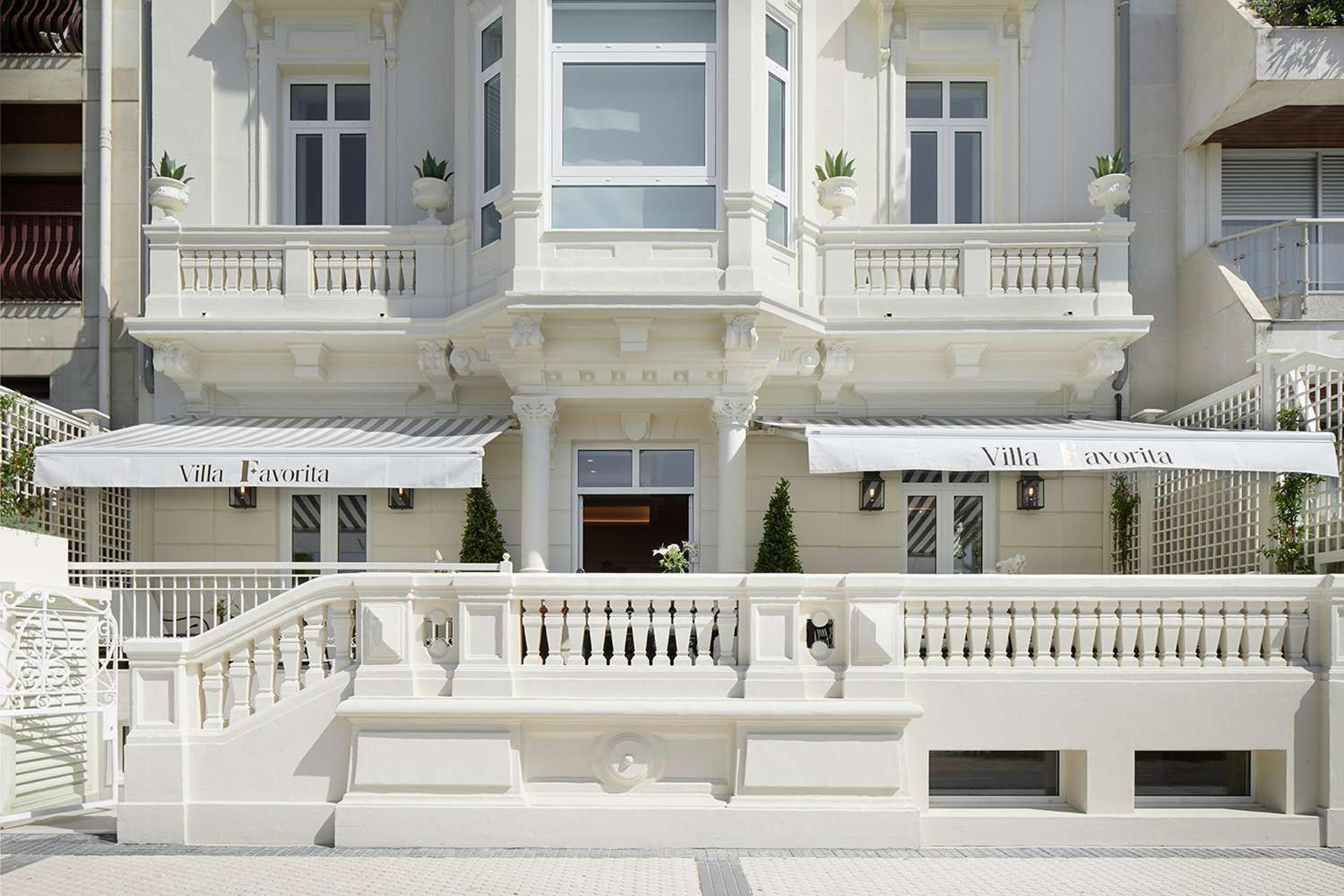 The hotel's white Belle Epoque facade with balconies, potted topiary, and awnings reading 'Villa Favorita'.