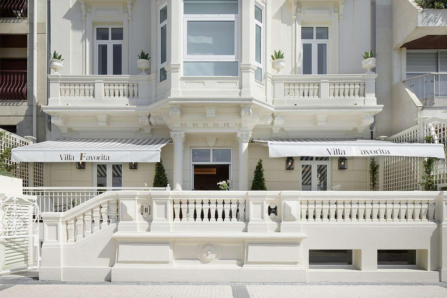 The hotel's white Belle Epoque facade with balconies, potted topiary, and awnings reading 'Villa Favorita'.